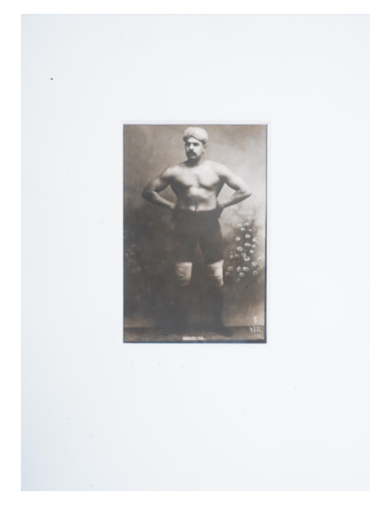 ANTIQUE RUSSIAN PORTRAIT PHOTO OF INDIAN WRESTLER: An antique Russian black and white photograph, depicting a studio portrait of Kahouta, an Indian Champion Wrestler. Circa: early 20th century. Titled, lower to the center. Marked in Cyrillic, YaR, and