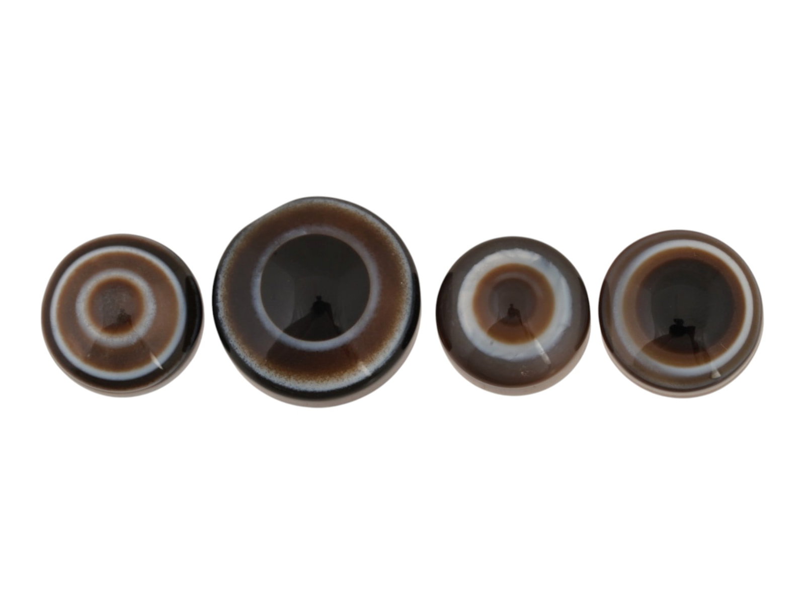 FOUR POLISHED BLACK AND BROWN BANDED AGATE CABOCHONS: A collection of four polished black and brown banded agate cabochons. The natural gemstones display striking concentric bullseye patterns with contrasting black, brown, and white banding,