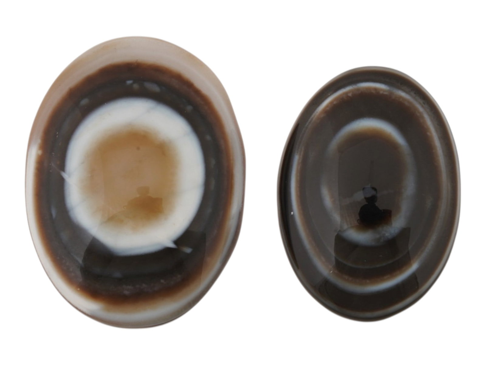LOT OF TWO NATURAL BULLSEYE BANDED AGATE CABOCHONS: A lot of two large banded agate specimen cabochons. Each is carved into an oval cabochon form, featuring a striking natural bullseye pattern. The pieces have been polished to a high luster on its