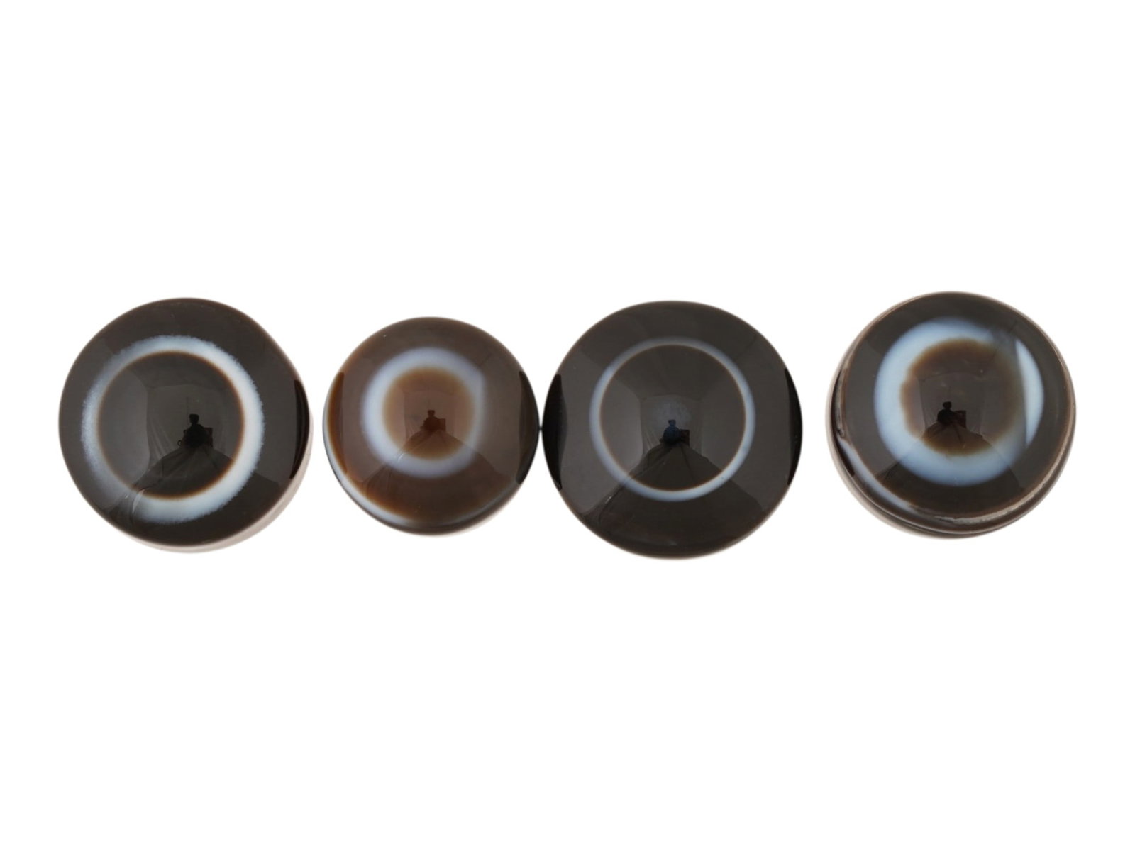 COLLECTION OF NATURAL BULLSEYE BANDED AGATE CABOCHONS: A collection of four large banded agate specimen cabochons. Each is carved into a circular cabochon form, featuring a striking natural bullseye pattern. The pieces have been polished to a high luster
