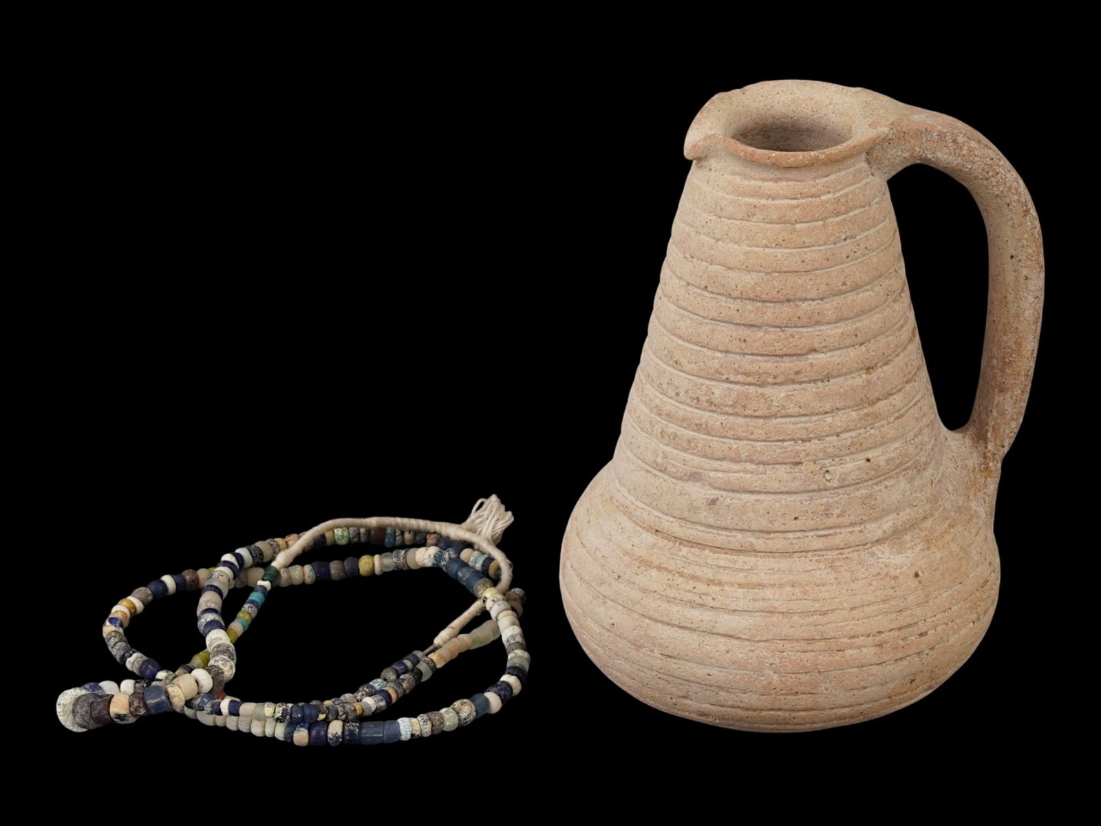 ANCIENT ROMAN WINE PITCHER AND GLASS BEAD NECKLACE: A group of ancient Roman artifacts dating to approximately 100 to 300 AD, including a terracotta wine pitcher and a glass bead necklace. The pitcher features a classic utilitarian form, while the neck