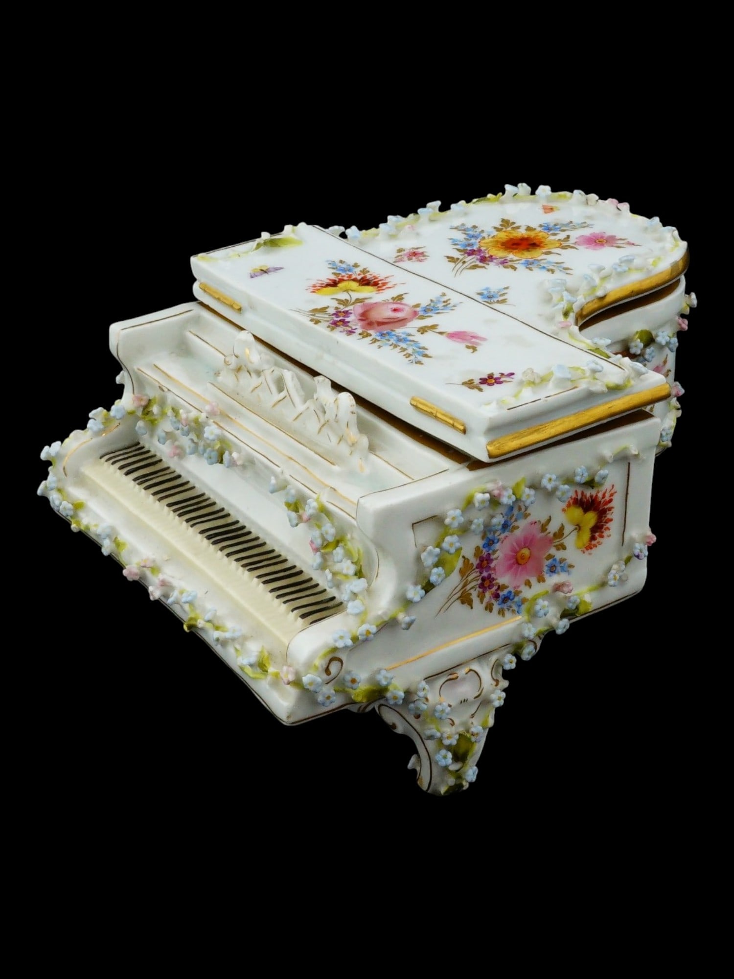 EIUROPEAN PIANO FLORAL PAINTED PORCELAIN FIGURAL BOX: A porcelain trinket box modeled in the form of a grand piano and features a white glaze decorated with hand painted polychrome floral sprays. The exterior is further embellished with high relief encru