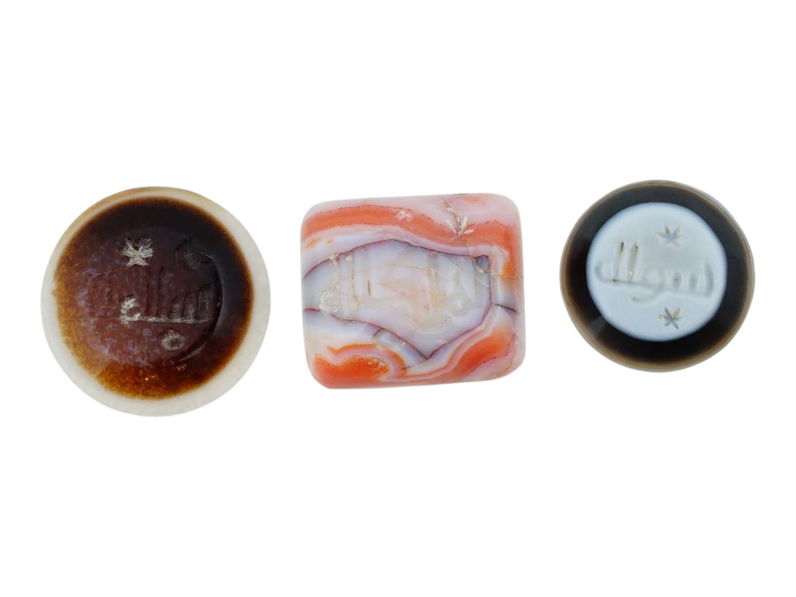 COLLECTION OF THREE ANTIQUE ISLAMIC INTAGLIO SEALS: A collection of three antique Islamic intaglio seals carved from banded and translucent agate, historically used as personal signets for stamping wax or ink. The left is a circular banded agate seal e