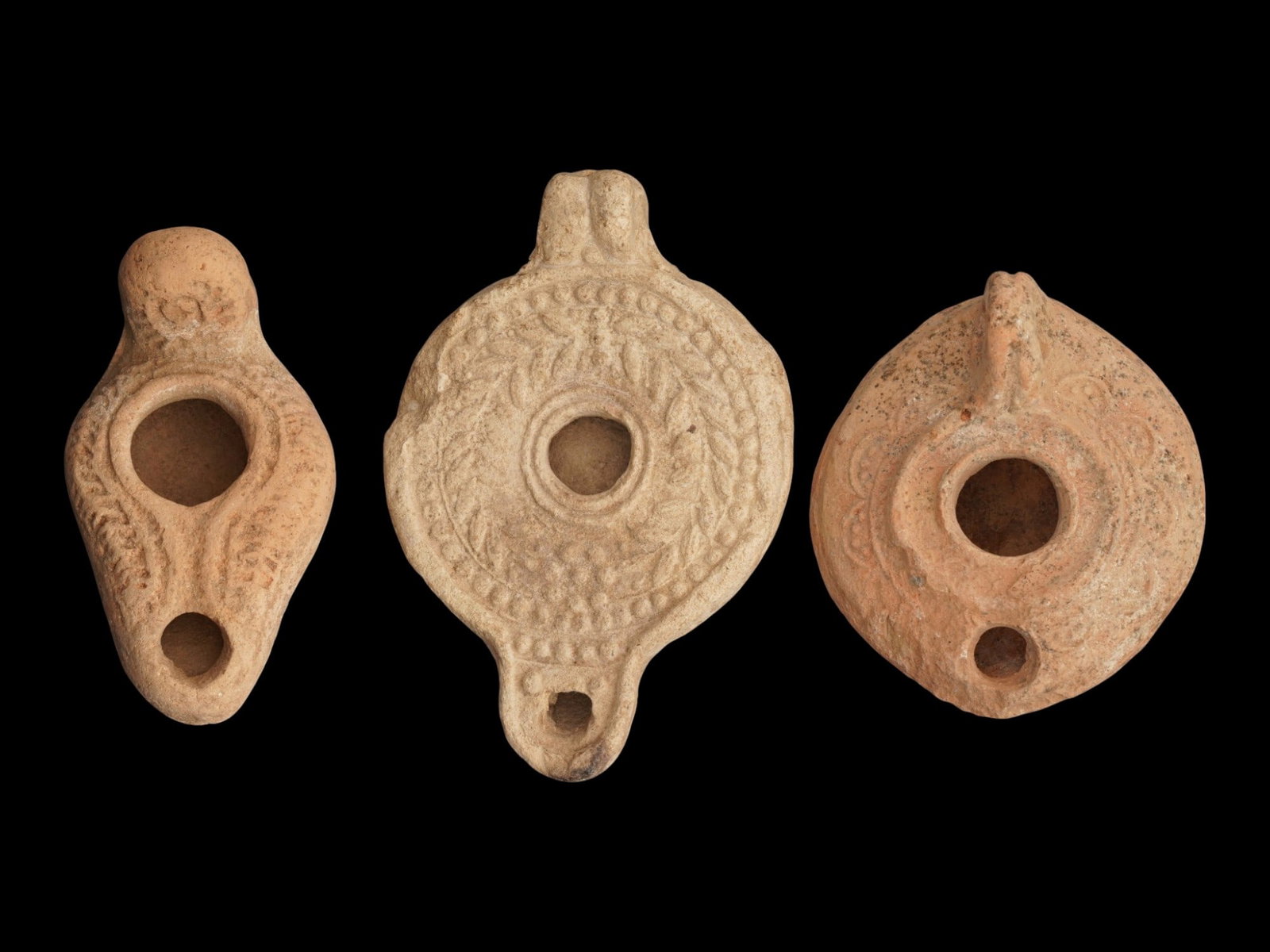LOT OF ANCIENT ROMAN BYZANTINE TERRACOTTA OIL LAMPS: A collection of three ancient Roman and Byzantine Empire terracotta pottery oil lamps. The first: an ancient Roman terracotta pottery oil lamp. The body of the lamp is adorned with engraved ornaments 
