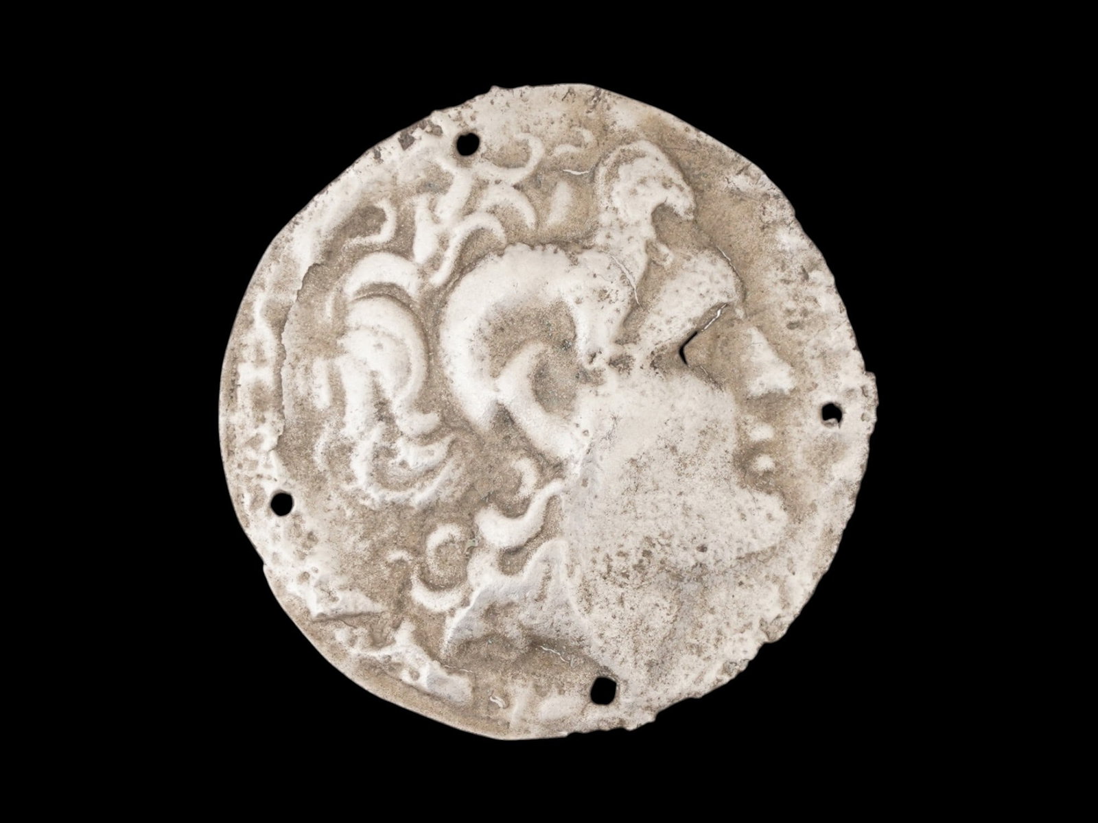 ANCIENT GREEK SILVER PLAQUE W PROFILE 400 TO 300 BC: An ancient Greek silver repousse plaque, circa 400 to 300 BC. The plaque features a right-facing profile, presumably the god or a leader. The small holes around the perimeter suggest it was intended t
