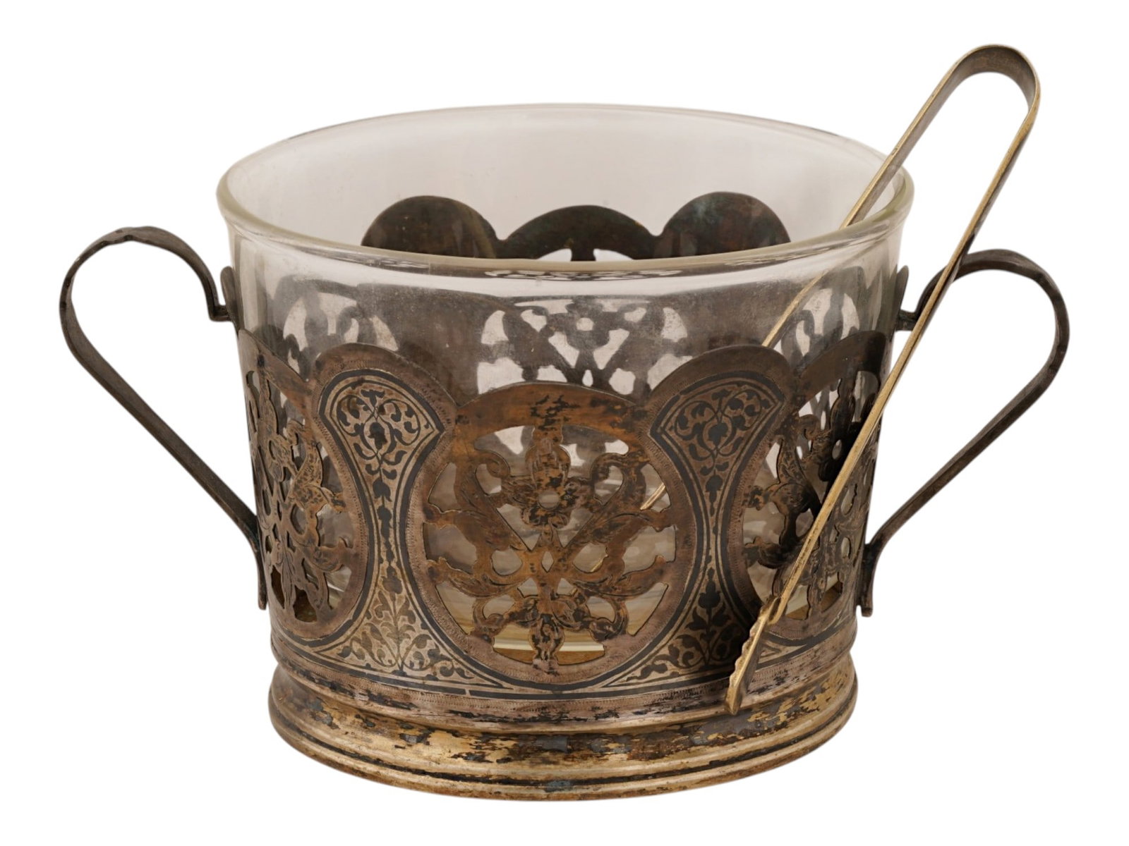 RUSSIAN GILT SILVER NIELLO GLASS HOLDER AND TONGS: A Russian silver gilt glass holder with a clear glass insert and a pair of matching tongs, all featuring intricate niello decoration. The holder is designed with a scalloped, pierced upper rim and dua