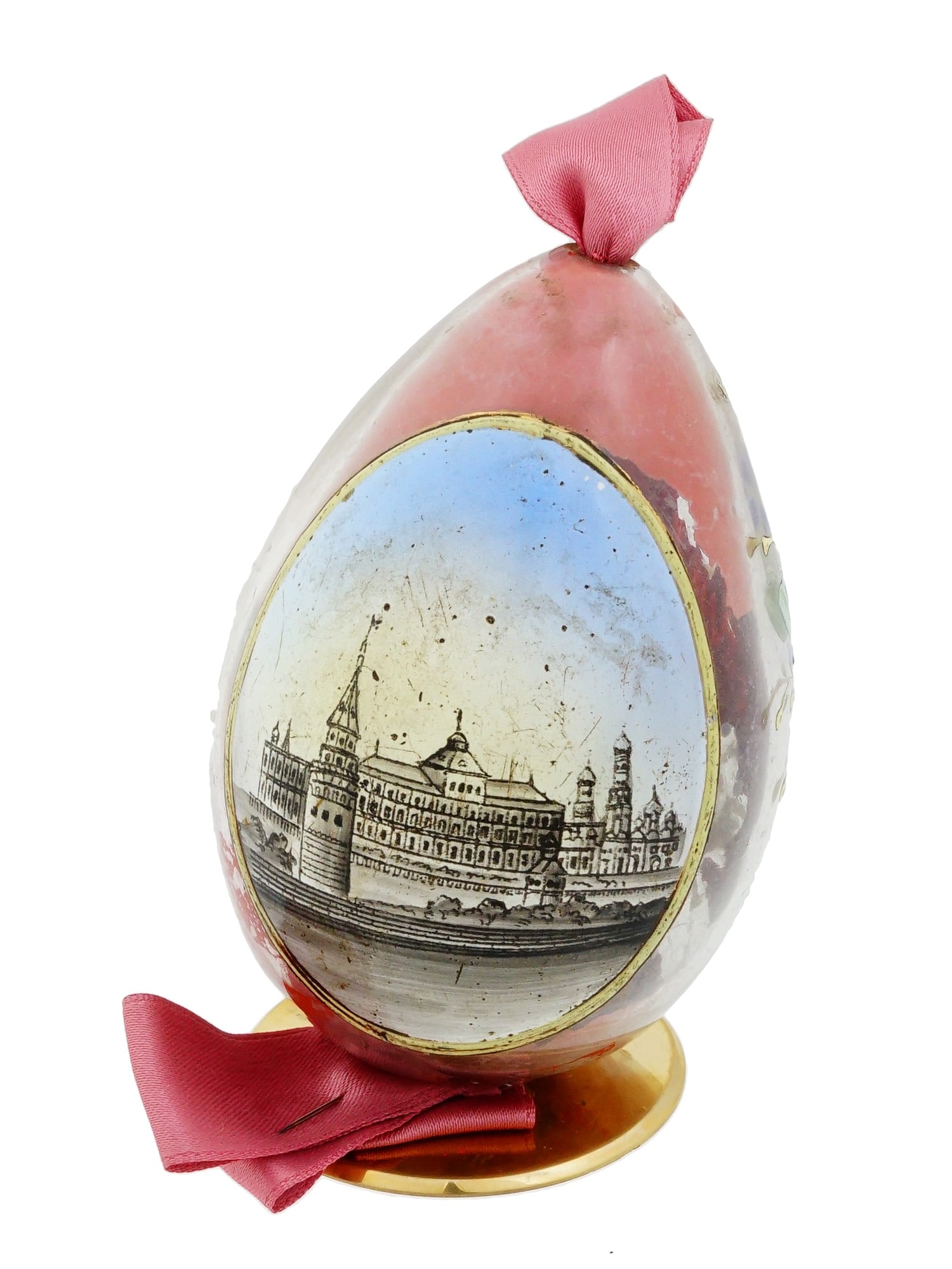 RUSSIAN MOSCOW KREMLIN ENAMEL GLASS EASTER EGG: A Russian glass Easter egg, crafted from glass featuring a vibrant rose colored ground and hand painted enamel decorations. The obverse presents a detailed topographical view of the Moscow Kremlin wit