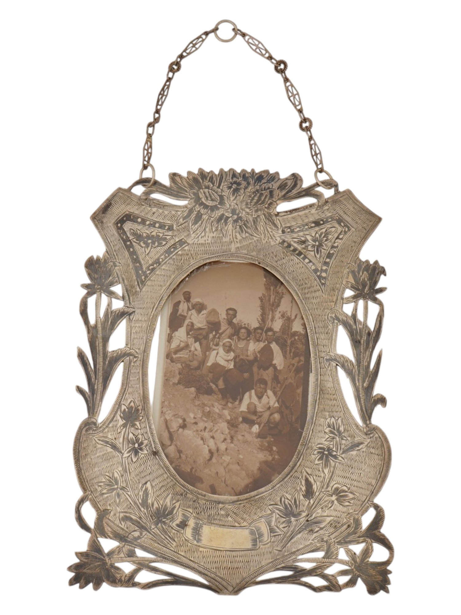 VINTAGE SILVER PICTURE FRAME WITH A GROUP PHOTOGRAPH: A vintage silver picture frame with a black-and-white group photograph. The openwork frame is decorated with flowing floral motifs, textured detailing, and a hanging chain for wall display. The