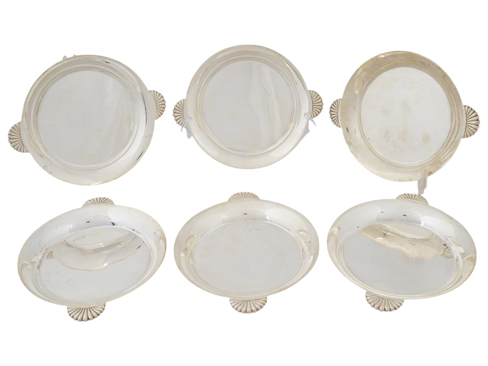 SET OF SIX METAL SERVING TRAYS W SEA SHELL HANDLES: A set of six metal serving trays. Small round trays with raised edges. Each has embossed handles on both sides reminiscent of sea shells. Traces of markings on the back of the handles. Collectible, Ta