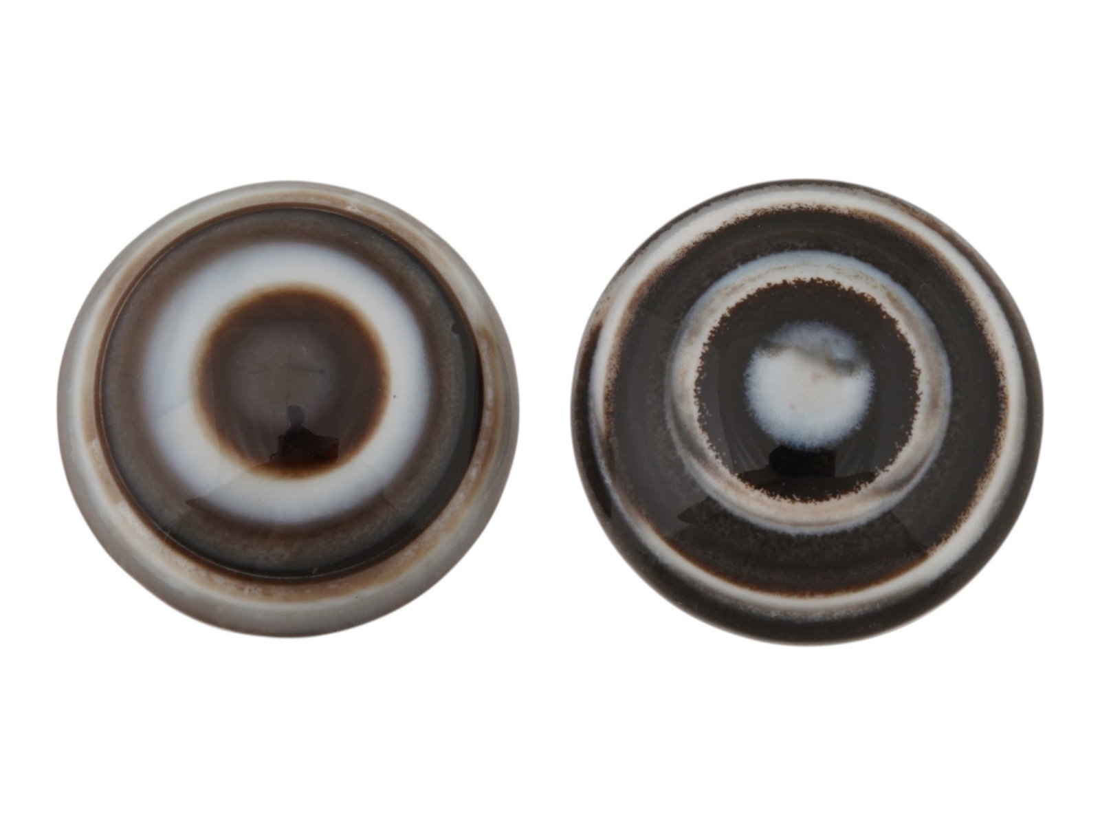 PAIR OF NATURAL BULLSEYE BANDED AGATE CABOCHONS: A pair of natural bullseye banded agate cabochons. The polished stones display concentric bands in shades of brown, black, cream, and white, creating the distinctive eye pattern. Natural Gemstones And