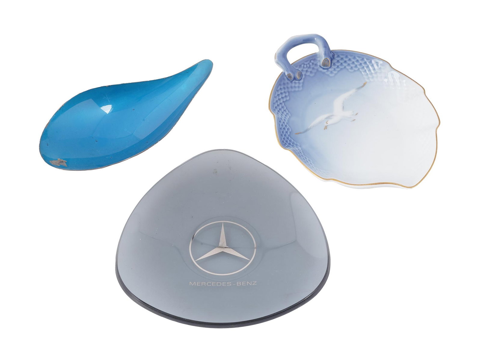 COLLECTION OF THREE PORCELAIN BRASS GLASS TRAYS: A collection of three various trays. The collection includes a clear glass tray, marked with a Mercedes Benz brand logo; a Reed and Barton covered blue silver plated tray in the shape of a curved drop
