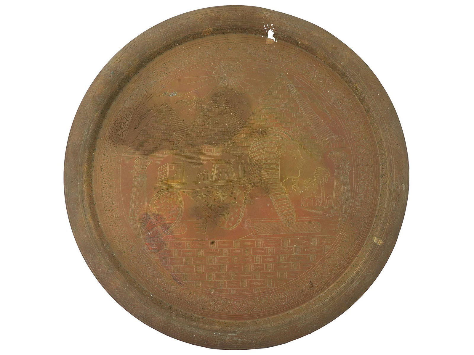 VINTAGE EGYPTIAN ROUND BRASS TRAY WITH ENGRAVED DECOR: A vintage Egyptian round brass tray, adorned with engraved decorations depicting a scene with a sphinx and pyramids. With intricate traditional decor to the rims. Circa the 1920s or 1930s. Vintage Dec
