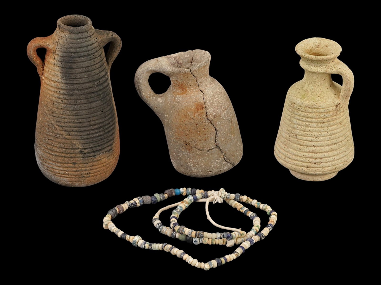 GROUP OF ANCIENT ROMAN JAR PITCHERS GLASS BEAD NECKLACE: A group of ancient Roman artifacts dating from approximately 100 to 300 AD, including one terracotta jar, two pitchers, and a colorful glass bead necklace. These pieces reflect the craftsmanship and e