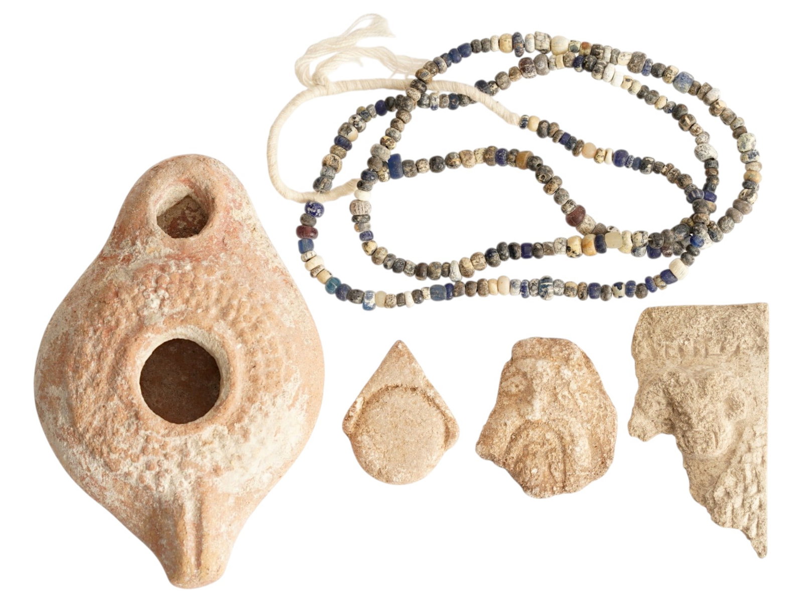 ANCIENT ROMAN OIL LAMP GLASS NECKLACE STONE FRAGMENTS: A lot of ancient Roman items including a terracotta oil lamp with a handle and patterned body, a multicolored glass bead necklace and a group of stone fragments with relief images. Dated circa 100 BC 