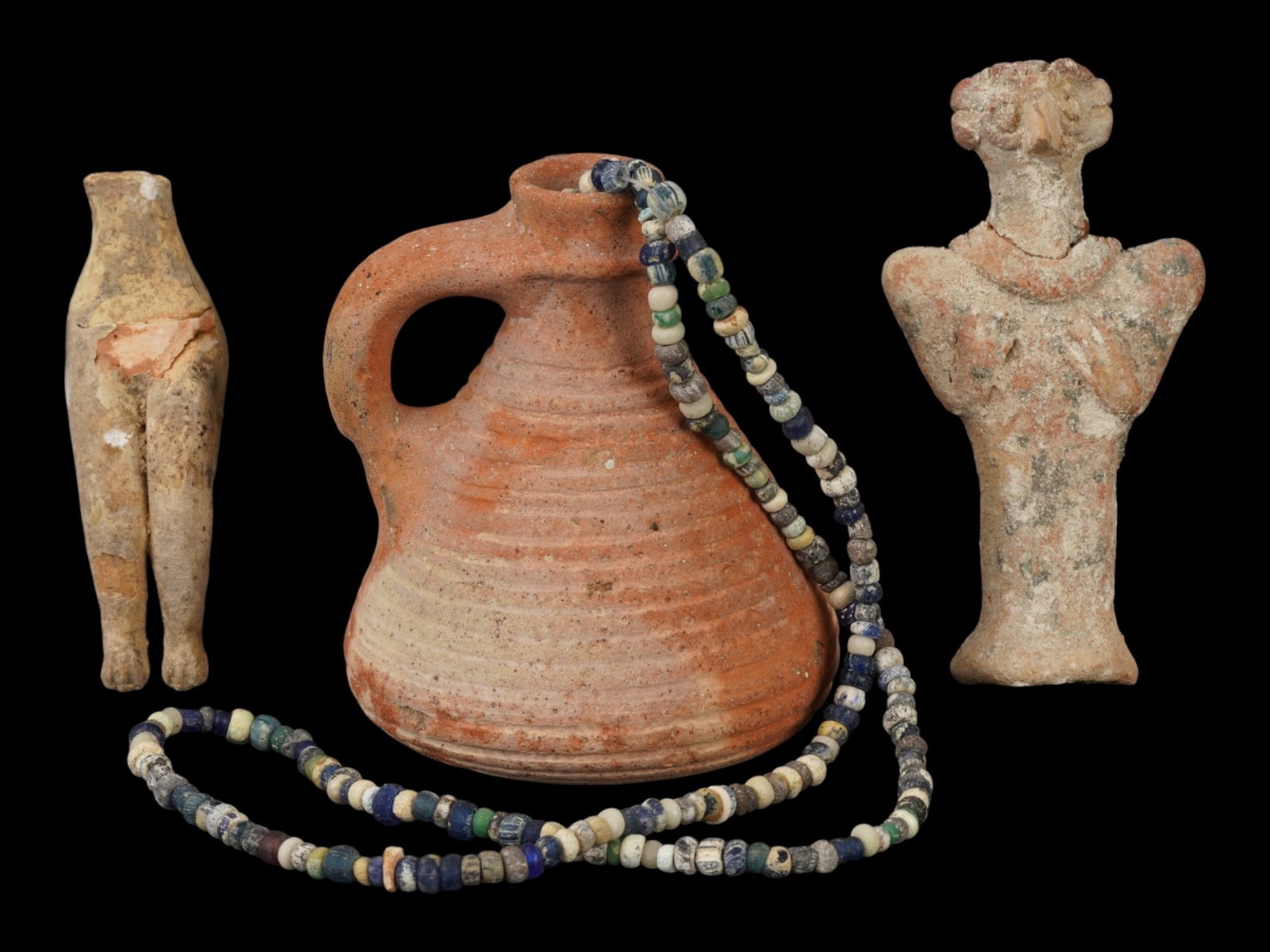 ANCIENT ROMAN TERRACOTTA AND GLASS ARTIFACTS 200 AD: A lot of Ancient Roman and earlier terracotta and glass artifacts. Imperial Rome era, ca. 200 AD. A total of four items. The lot contains a glass beaded necklace, a terracotta pitcher, and two figurin