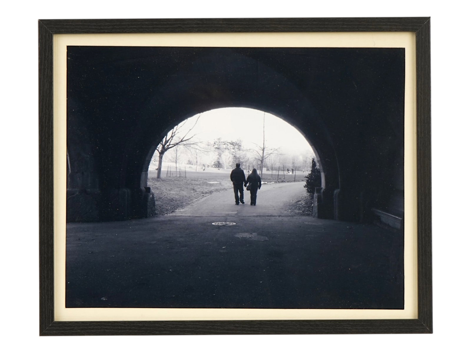AMERICAN NEW YORK PARK STREET SCENE BW PHOTO FRAMED: A black and white professional photograph depicting a couple in silhouette walking away through a stone archway, set within a New York City park landscape. Framed. A handwritten note on the cardboard 