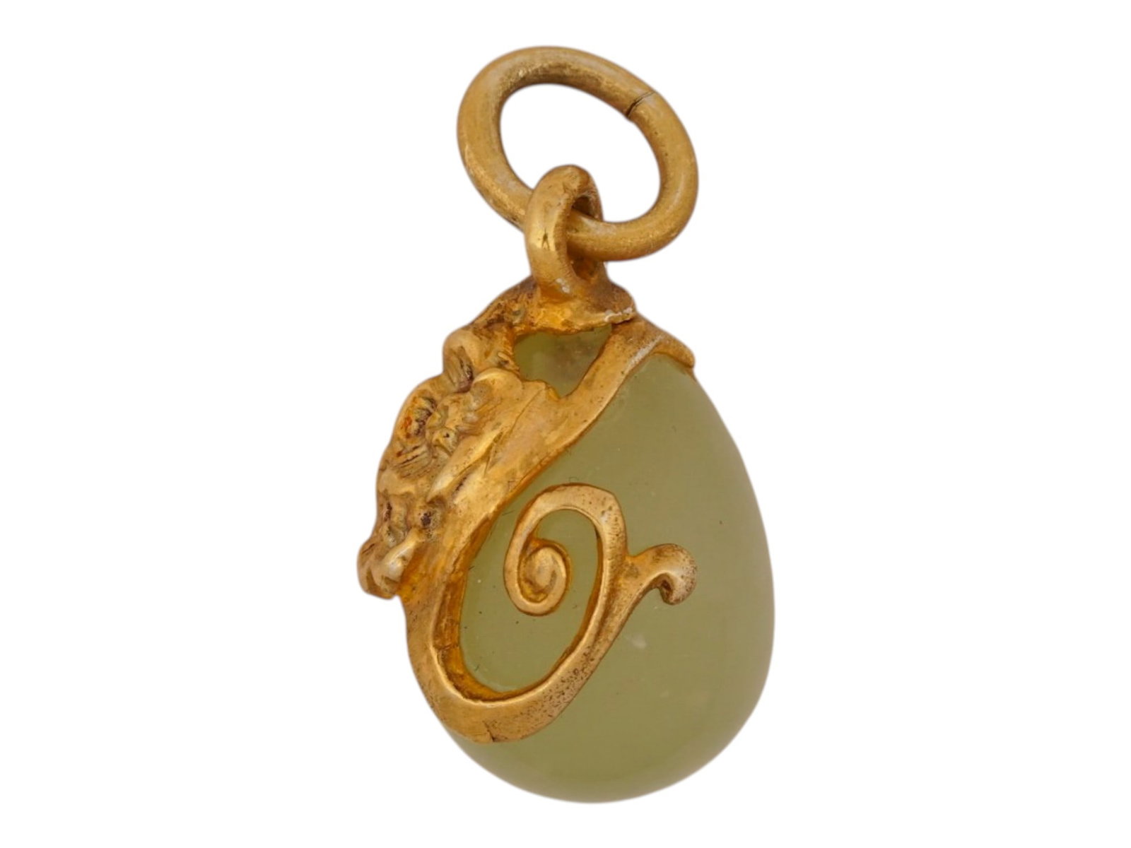RUSSIAN GILT SILVER CARVED BOWENITE EASTER EGG PENDANT: A Russian gilt silver and carved bowenite Easter egg pendant, featuring a pale apple-green hardstone body and a jeweled mount. The egg is topped with chased silver in an Art Nouveau floral design,
