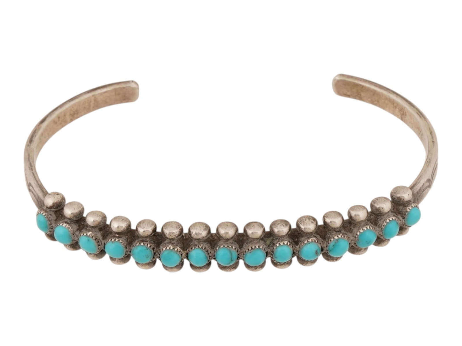 AMERICAN SILVER CUFF BRACELET WITH TURQUOISE STONES: An American cuff bracelet crafted in silver. The bracelet features fifteen small turquoise cabochons arranged in a linear row. Each stone is housed within an individual bezel setting, flanked by