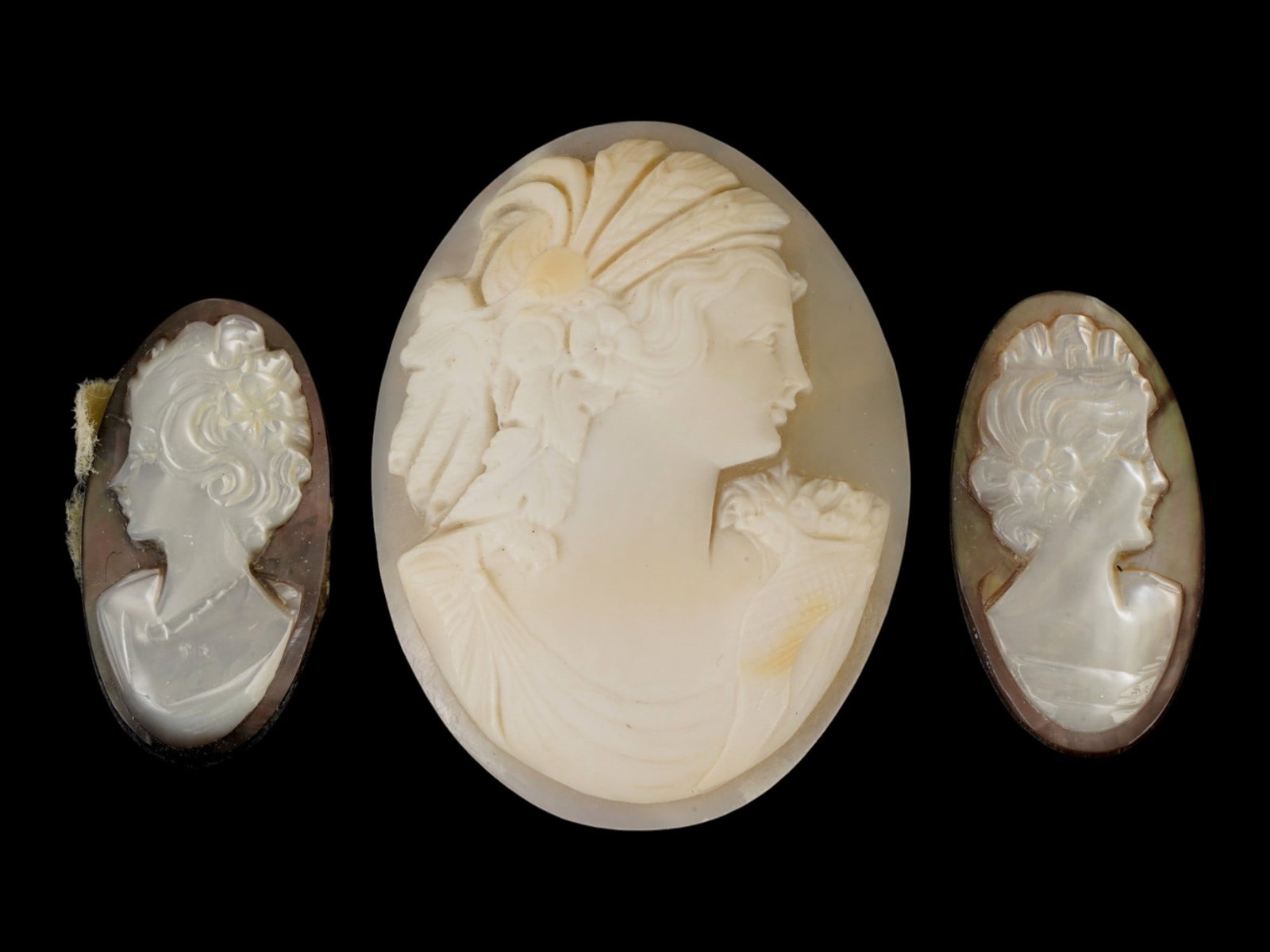 LOT OF CARVED FEMALE PORTRAIT SHELL CAMEO MEDALLIONS: A collection of three hand carved shell cameo medallions. The pieces depict a female profile portrait rendered in high relief in the Victorian and Roman manners. Each cameo is fashioned in a distincti