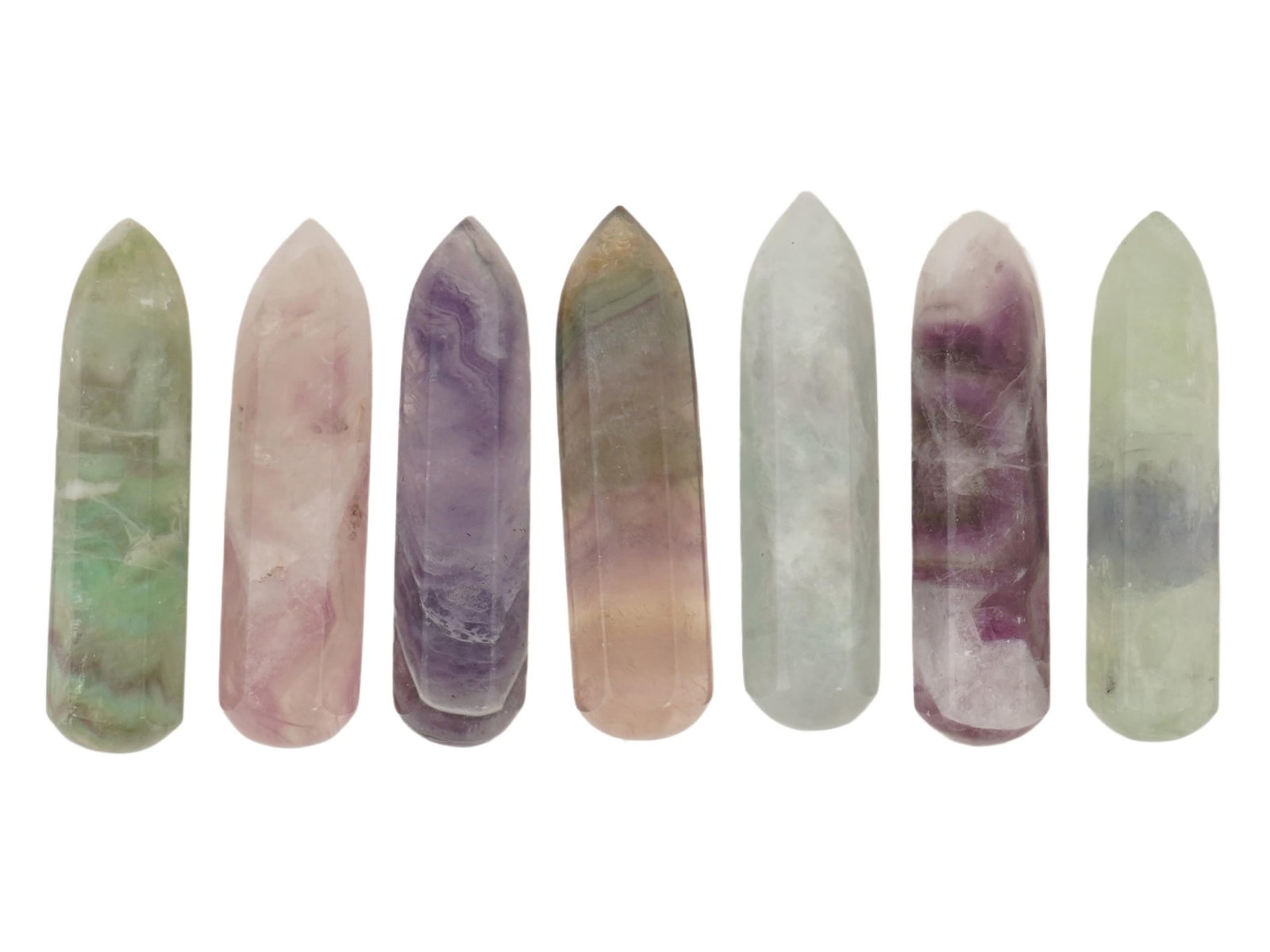 GROUP OF SEVEN CARVED POINTED FLUORITE STONES: A group of seven carved fluorite pointed stones. Shades of purple, pink, green, white, and blue are intertwined in unique patterns, creating a sense of harmony. Modern and Vintage Carved Natural Stone
