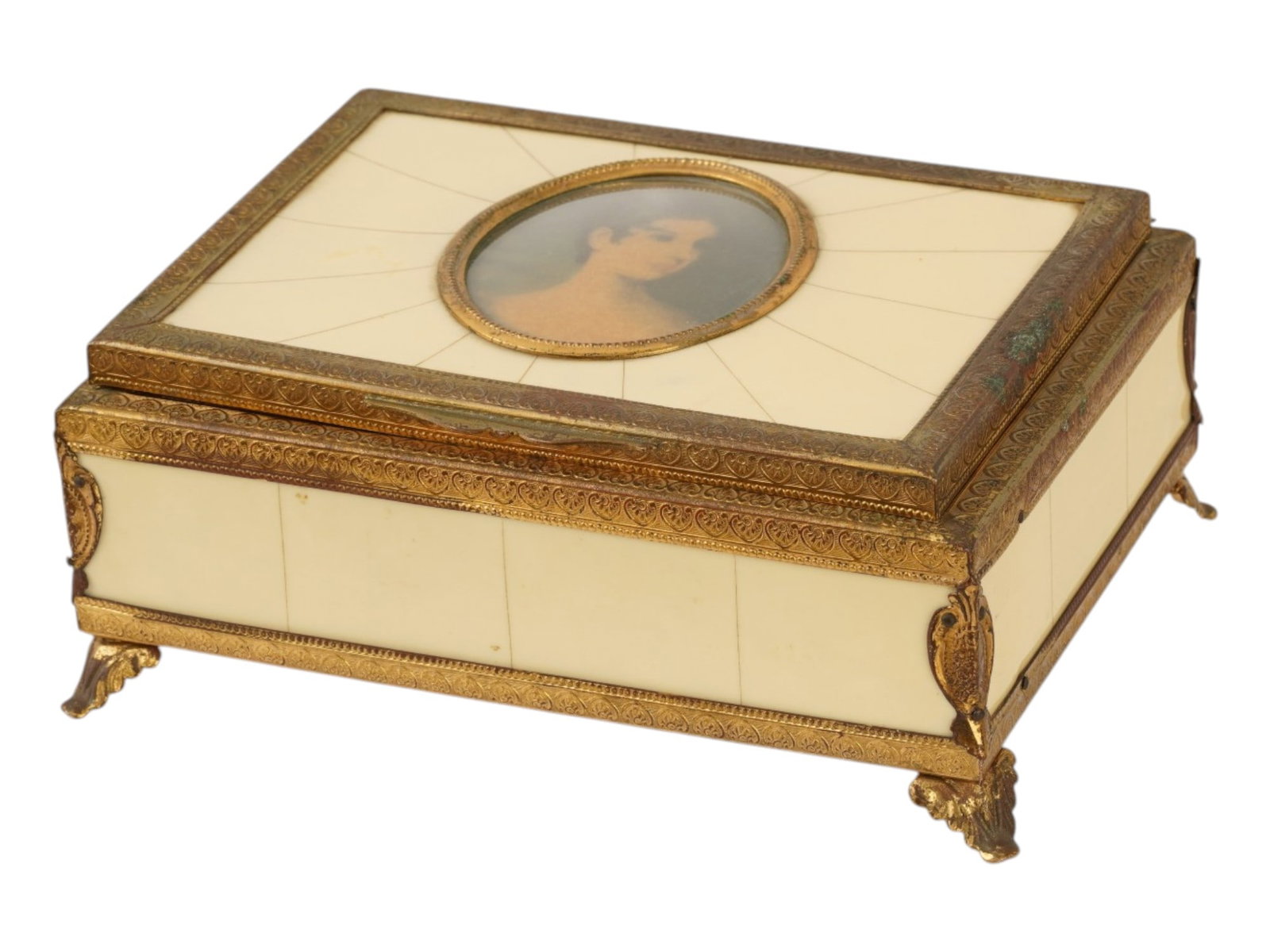 VINTAGE ARGENTINE BRASS BAKELITE PORTRAIT MUSIC BOX: A vintage Argentine trinket or jewelry box with a musical mechanism. Ivory-color bakelite body with brass rims and feet in relief acanthus leaf motif. The hinged lid is embellished with a color female