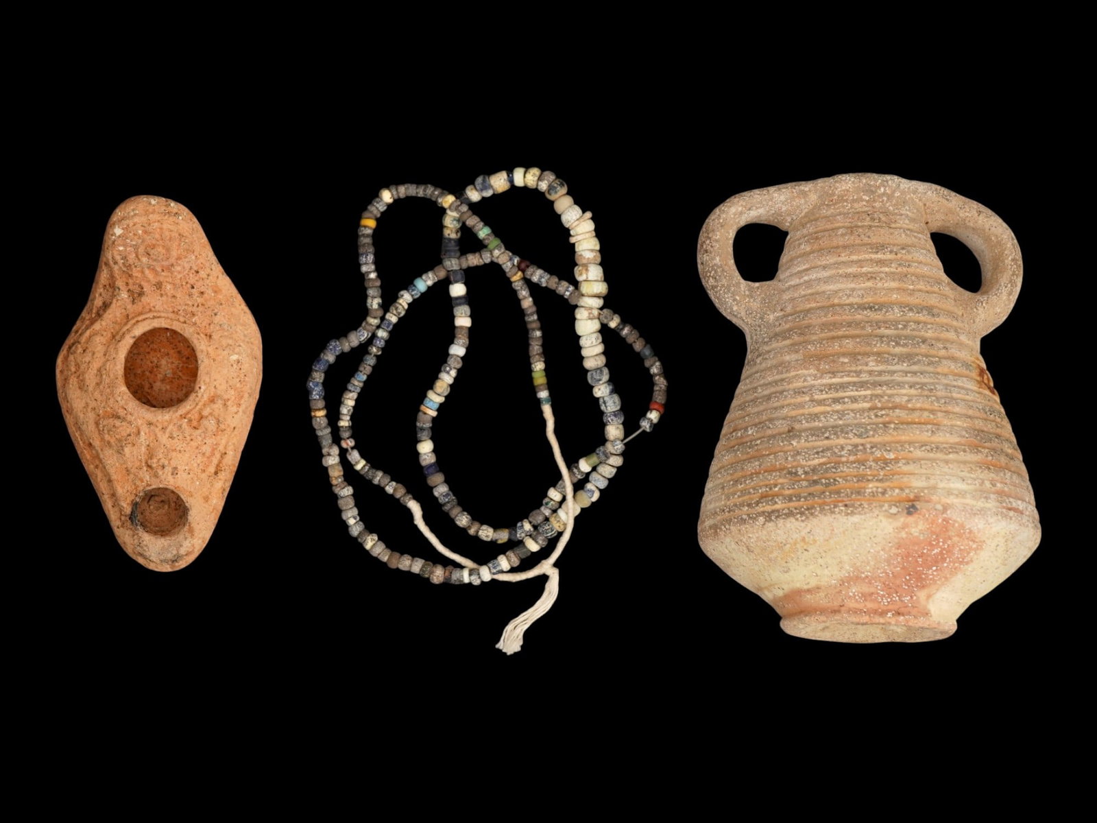LOT OF ANCIENT ROMAN BEADED NECKLACE OIL LAMP VESSEL: A lot of three Ancient Roman artifacts. Imperial Rome era, ca. 100 to 300 AD. The lot includes a glass beaded necklace and a terracotta pottery oil lamp decorated with an eye on the handle and grapes 