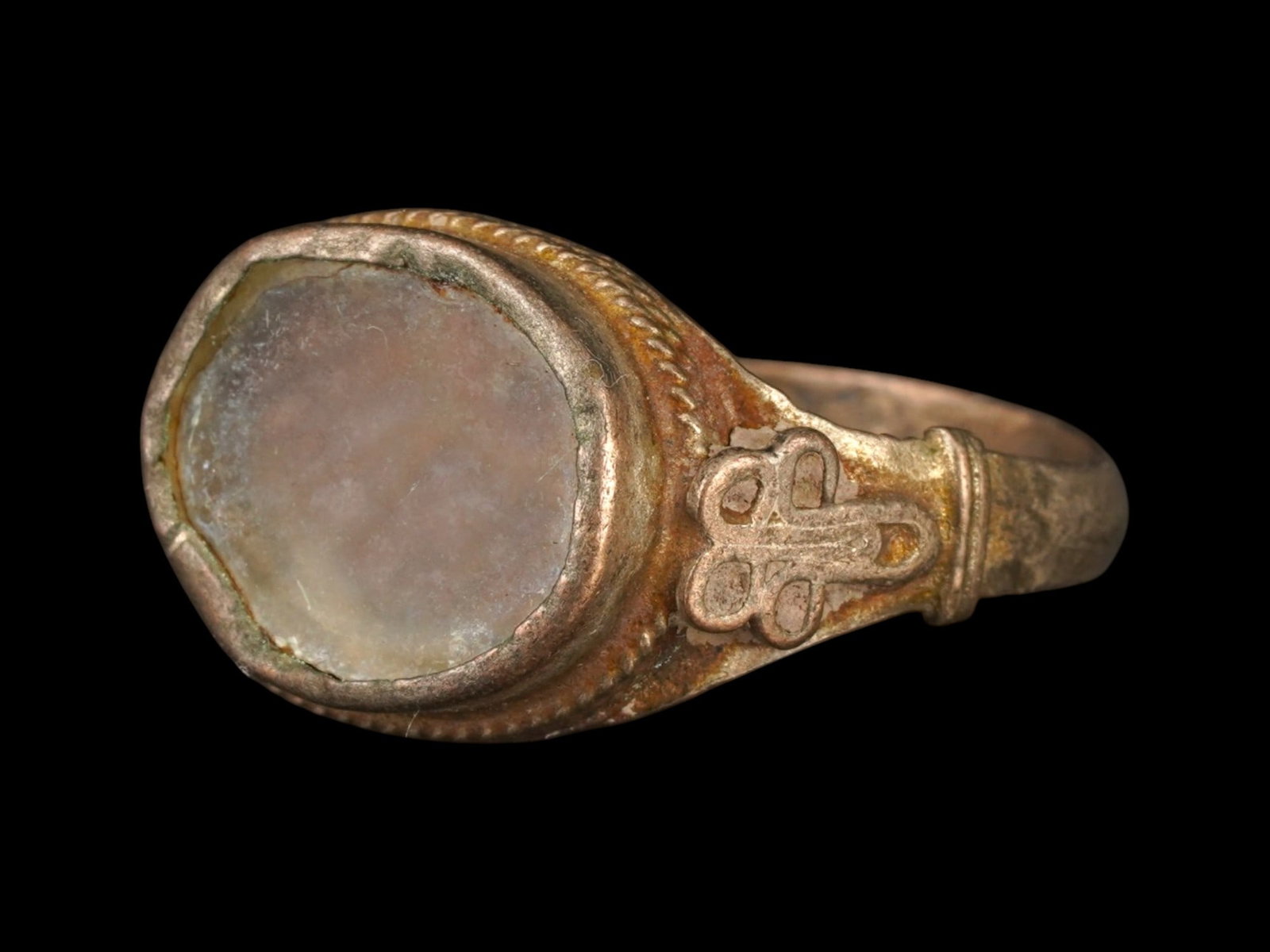 ANCIENT ISLAMIC SILVER RING W GLASS 600 TO 800 AD: An ancient Islamic silver ring, dating from 600 to 800 AD, featuring a bezel inlaid with glass and a braided pattern around the center with relief decorative details on the sides. Ancient Islamic Ring