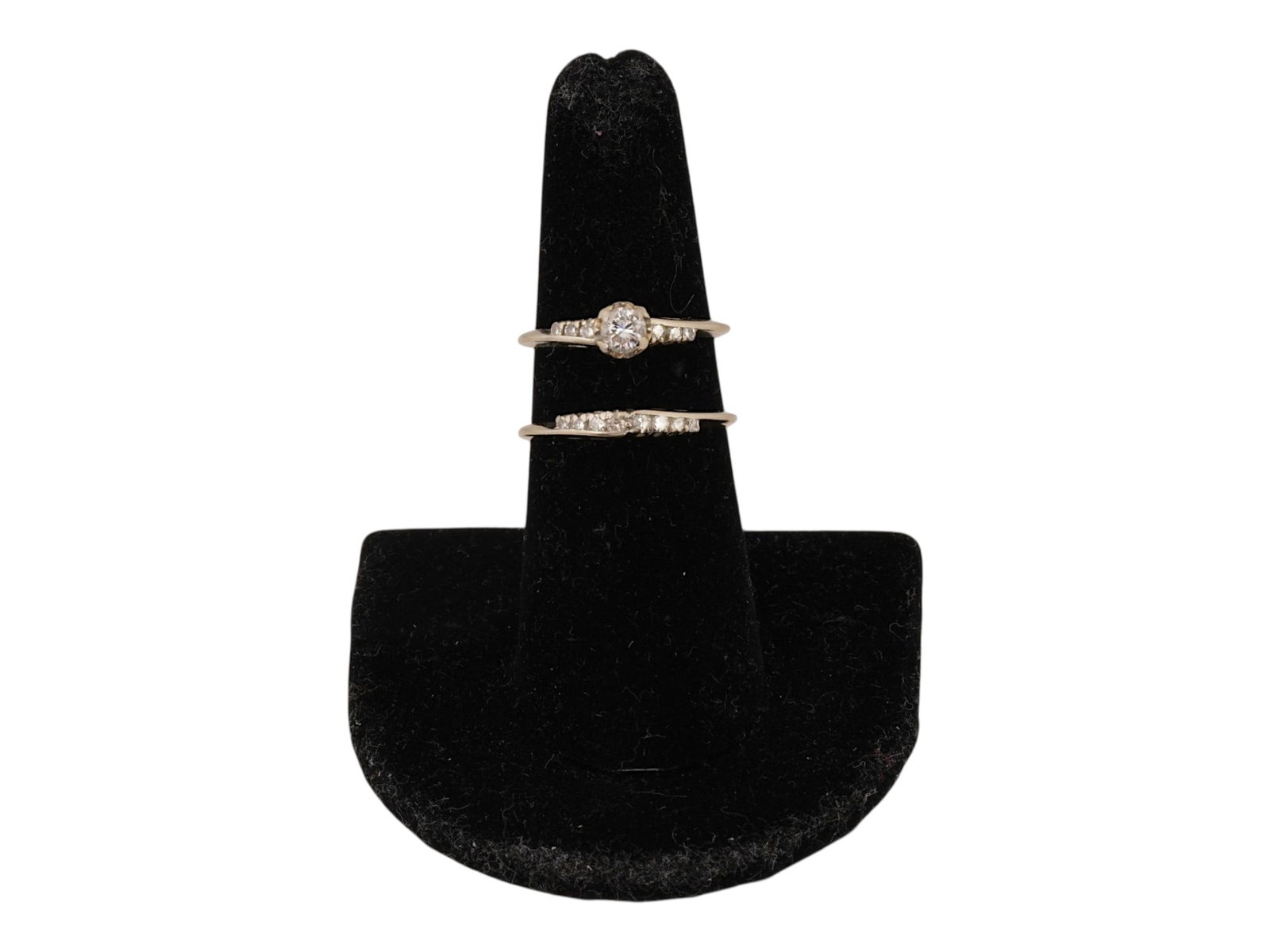TWO 14K WHITE GOLD RINGS WITH DIAMONDS: A lot of two 14k white gold rings with diamonds. The first ring features a large raised center stone surrounded by several smaller diamonds. The second ring features a diamond line of the same size. B