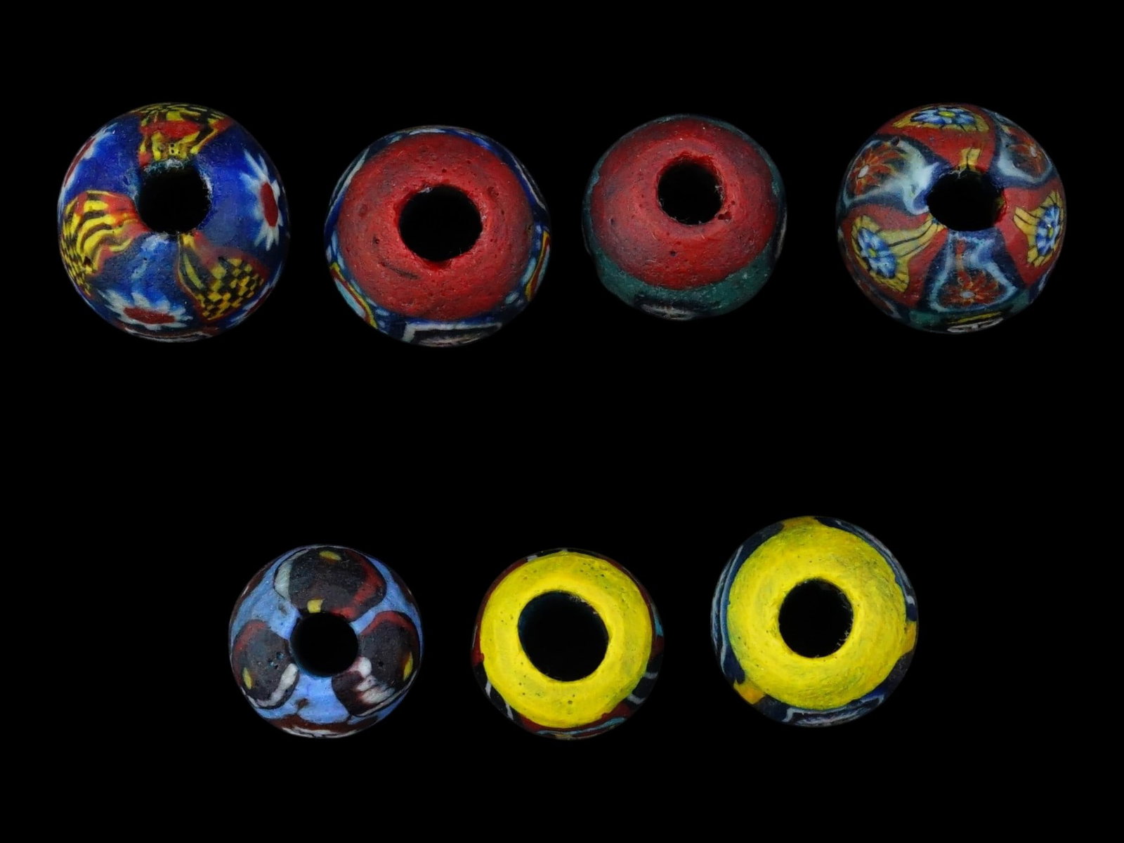 COLLECTION OF VENETIAN MILLEFIORI MOSAIC GLASS BEADS: A collection of seven glass beads crafted using the millefiori mosaic technique, featuring distinct polychrome canes that depict human faces. Each bead is embellished with intricate floral and geometr