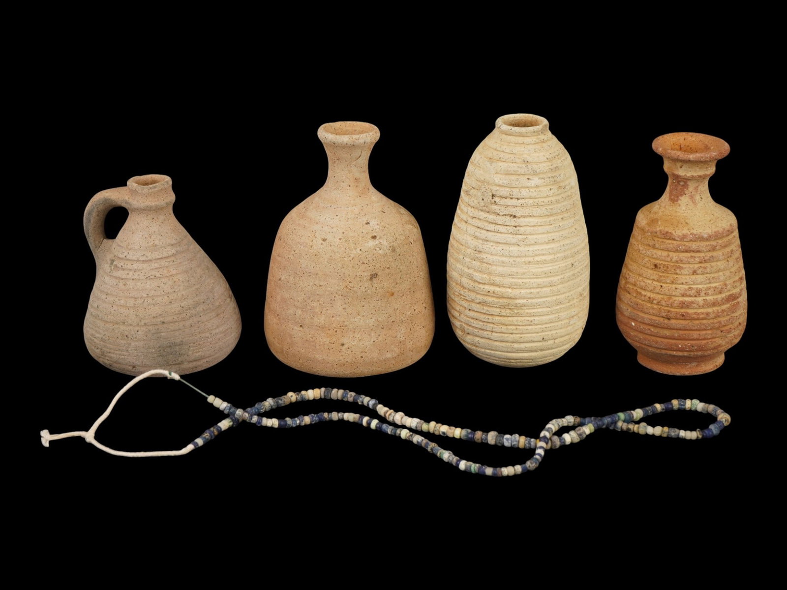 ANCIENT HOLY LAND TERRACOTTA VESSELS AND GLASS NECKLACE: A group of ancient Holy Land terracotta vessels accompanied by a glass bead necklace, dating to the Roman or Byzantine period, circa 100 to 500 AD. The assemblage reflects the everyday ceramic and per