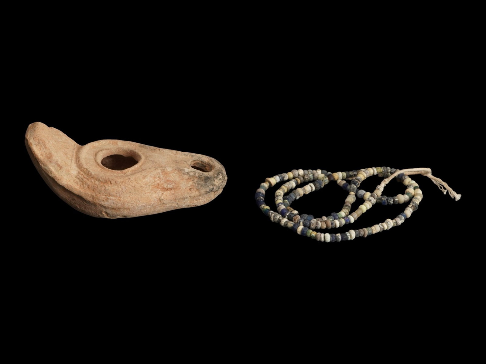 ANCIENT JUDAICA TERRACOTTA OIL LAMP ROMAN GLASS BEADS: An ancient Judaica terracotta oil lamp with a temple doorway motif on the handle, dating to the Late Roman or Early Byzantine period, circa 300 to 500 AD, accompanied by a strand of ancient glass bead