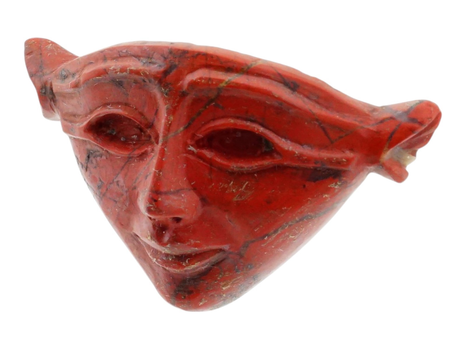 ANCIENT EGYPTIAN RED JASPER INLAY GODDESS HATHOR FACE: An ancient Egyptian red jasper inlay depicting the stylized face of the goddess Hathor, identified by her characteristic human features and prominent cow ears. The finely carved face features almond-s
