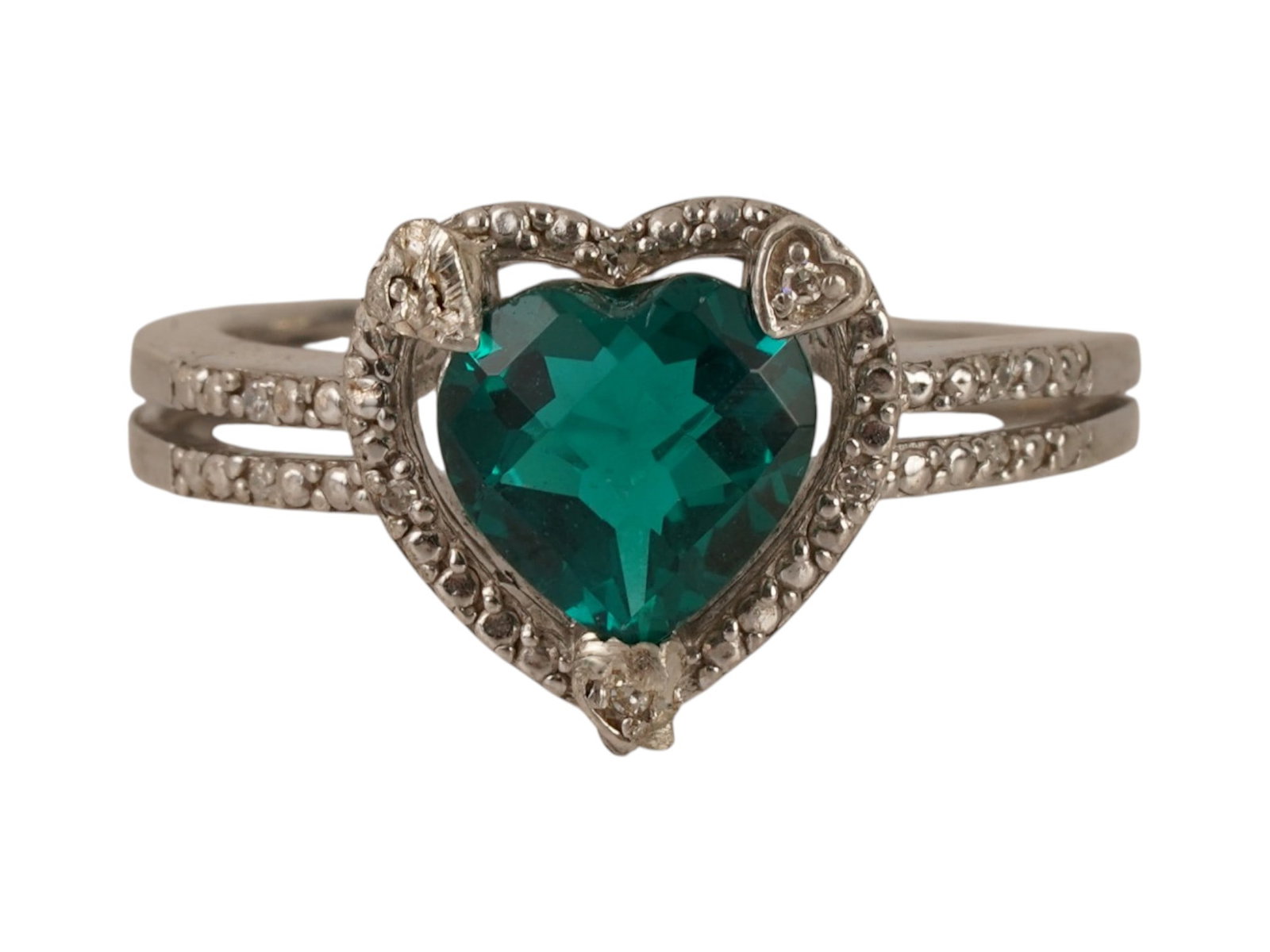 STERLING SILVER HEART SHAPED GREEN GEMSTONE RING: A heart shaped emerald ring is crafted from sterling silver or white gold and features a prominent, faceted green gemstone nestled inside a decorative metal border. The split shank band is accented wi