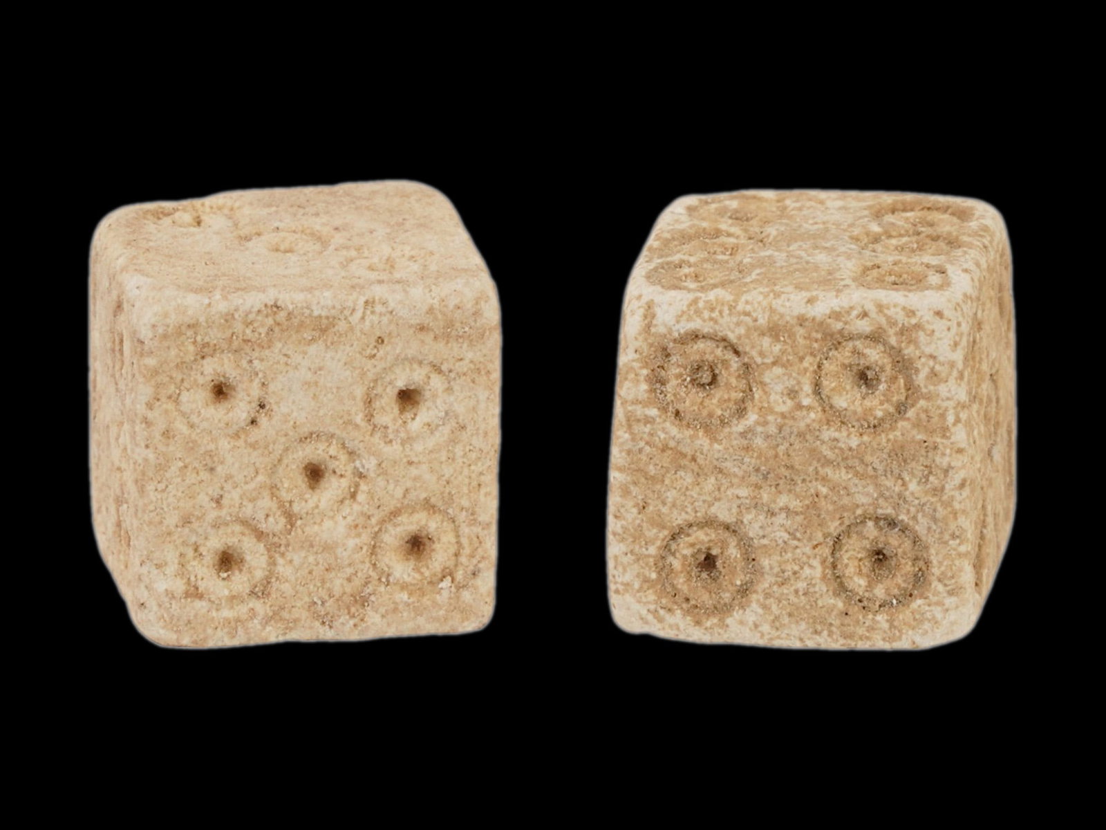 PAIR OF ANCIENT ROMAN STONE DICE 100 TO 300 AD: A pair of ancient Roman hand carved stone dice, dating from 100 to 300 AD. These artifacts offer a tangible connection to the everyday life and leisure activities of the past. Carved from stone featur