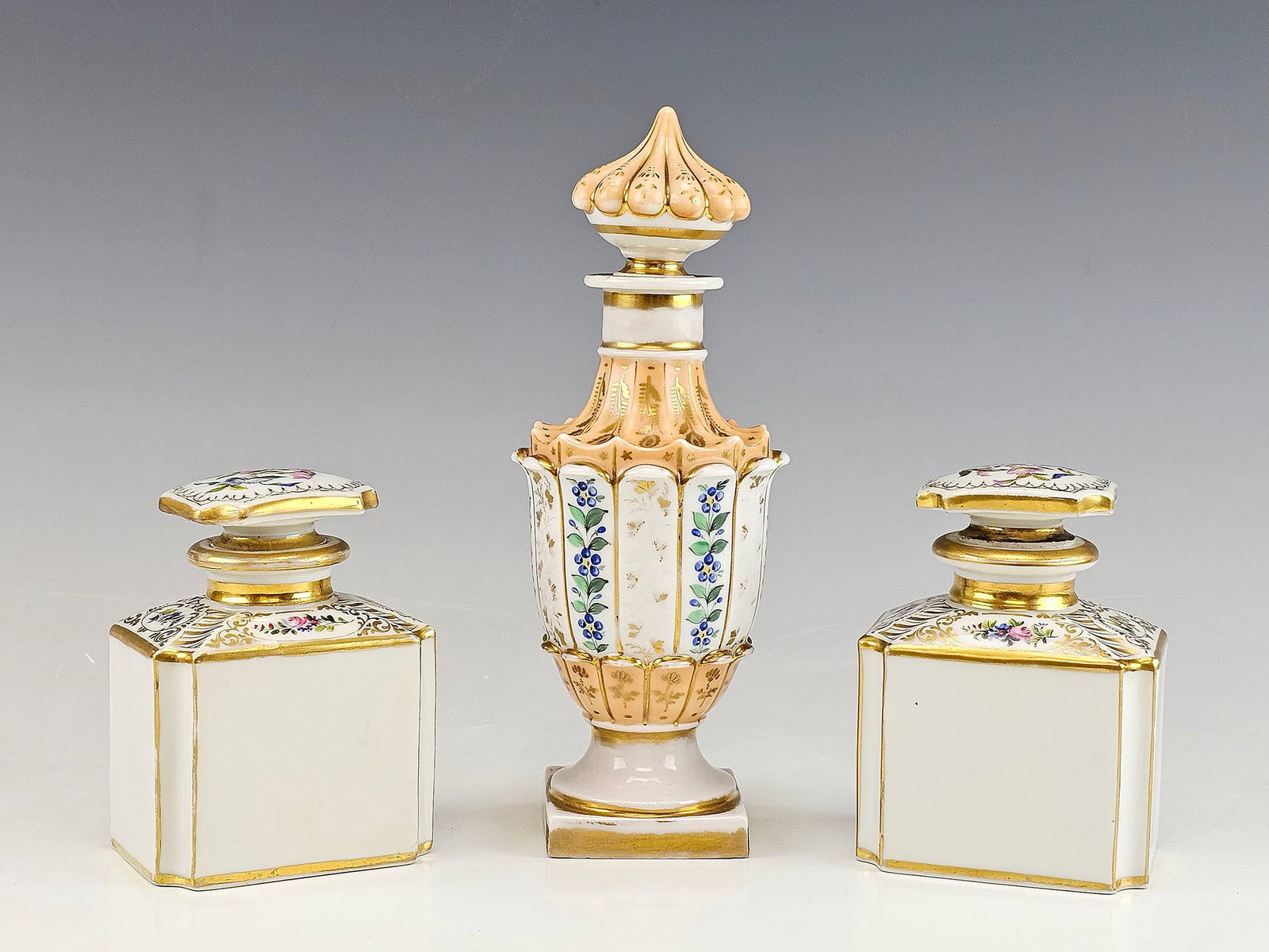 ANTIQUE FRENCH SEVRES STYLE PORCELAIN PERFUME BOTTLES: A set of three antique 19th-century French porcelain perfume bottles in the Sevres style. The bottles feature hand painted floral and gilt decoration. The taller bottle has an elegant shape with a fla