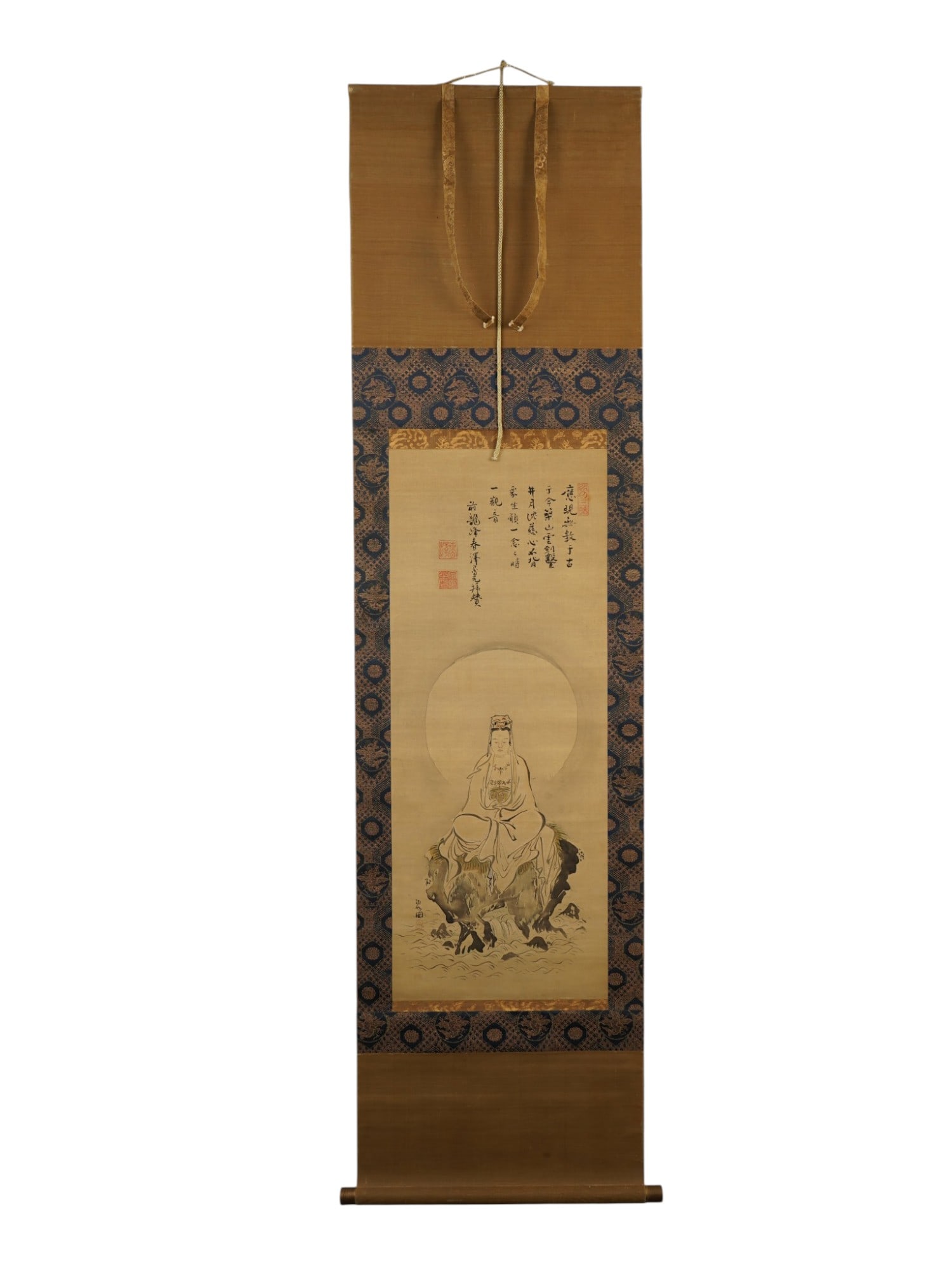 JAPANESE KANNON PORTRAIT INK PAINTING HANGING SCROLL: A Japanese hand painted hanging scroll depicting Kannon seated upon a rocky outcrop amidst swirling waves, rendered in monochrome ink. The deity is shown with a large circular halo, wearing flowing ro