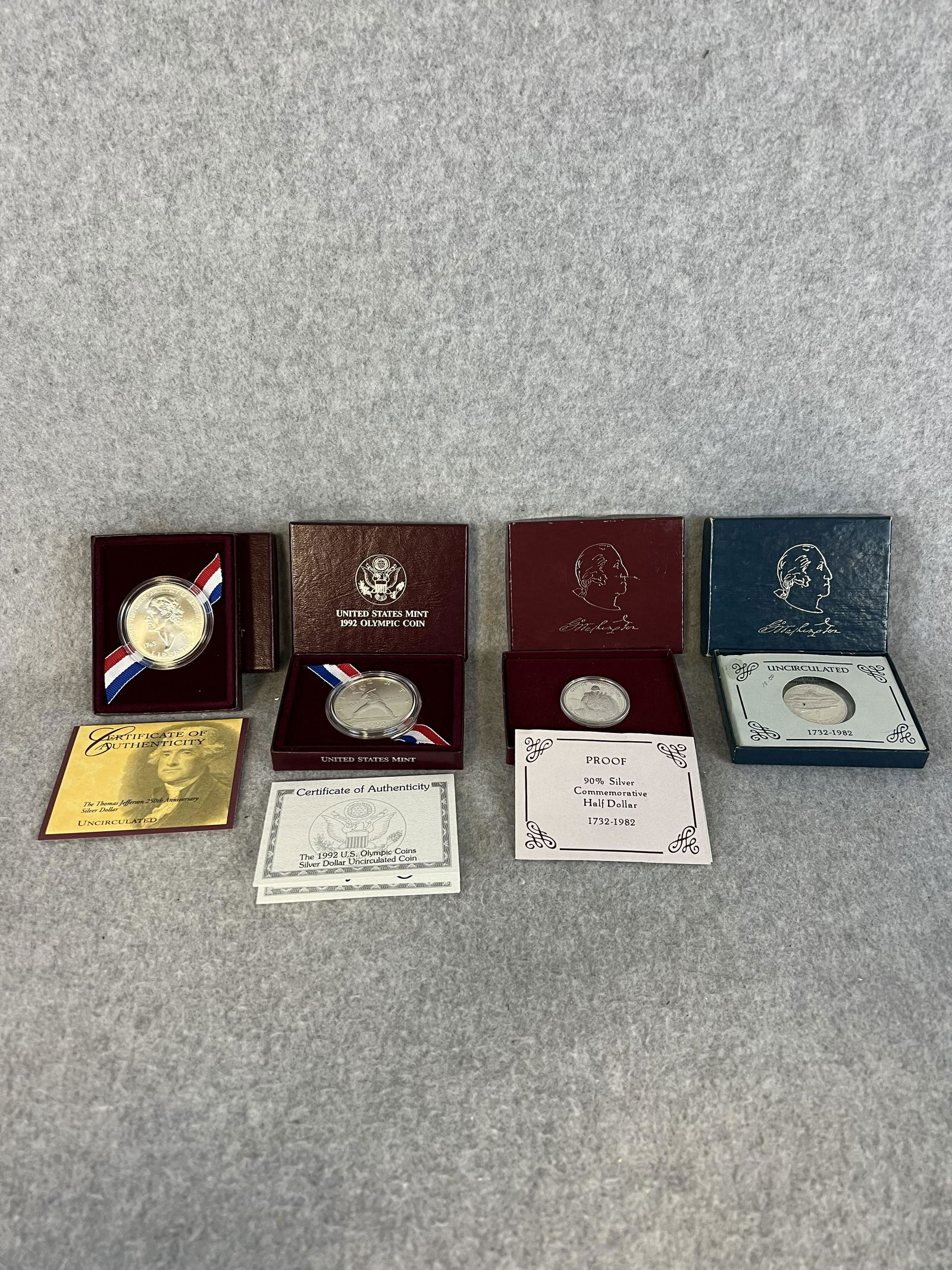 Lot 4 Silver US Mint Coins w Boxes/ COA's: A lot of four silver US Mint coins to include; 1992 Olympic uncirculated silver dollar, 1993 Thomas Jefferson uncirculated silver dollar, 1982 silver half dollar and the 1982 George Washington proof h