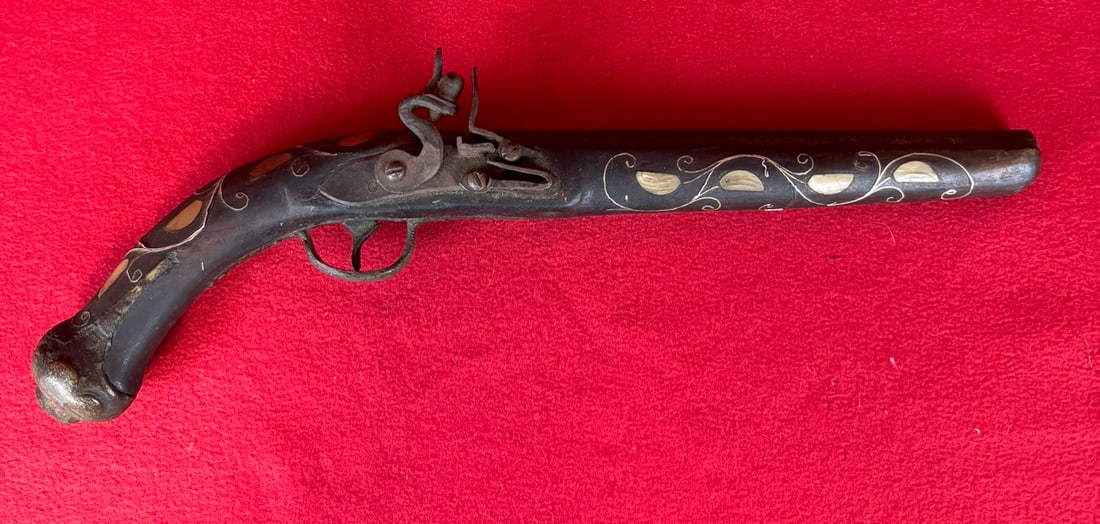 Early Inlaid Flintlock Pistol: Early inlaid flintlock pistol the stock of which is inlaid with silver wire and horn in a floral or vine type pattern. The trigger guard and butt plate are crudely cast of brass. The flintlock mechani