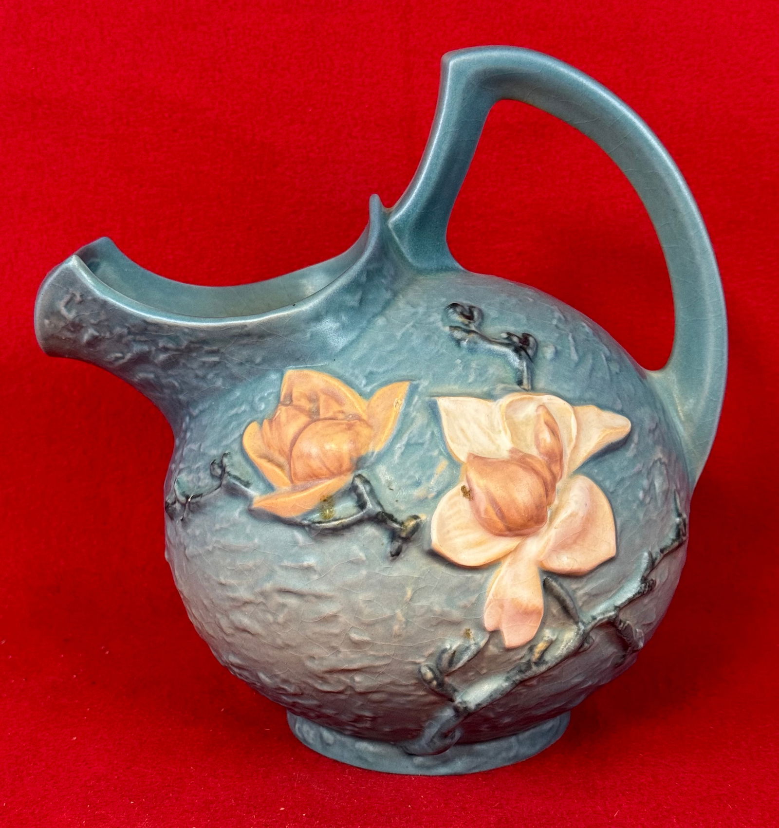 Roseville Blue Magnolia 132 7 Cider Pitcher: Original Roseville 132 7 cider pitcher with pour lip in the Magnolia pattern which dates to 1943. Pitcher is marked on underside of the base in relief Roseville / U.S.A. / 132 7 and is in the blue col
