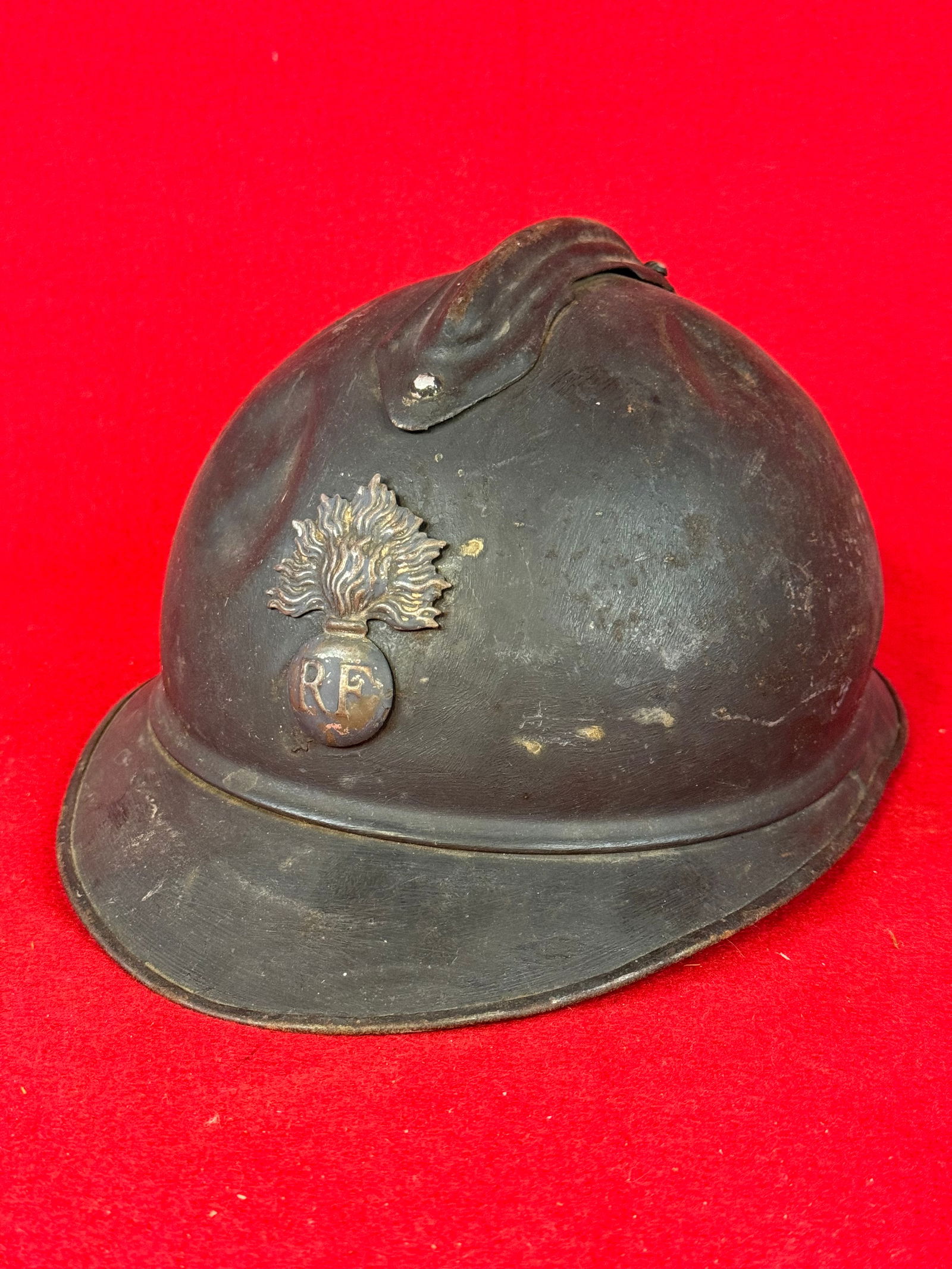 French Model 26 "Adrian" Helmet With Battle Damage: French Model 26 "Adrian" combat helmet with infantry flaming bomb insignia on front and dark gray finish. Helmet exhibits battle damage in the form of several dents . Helmet has its liner but only par