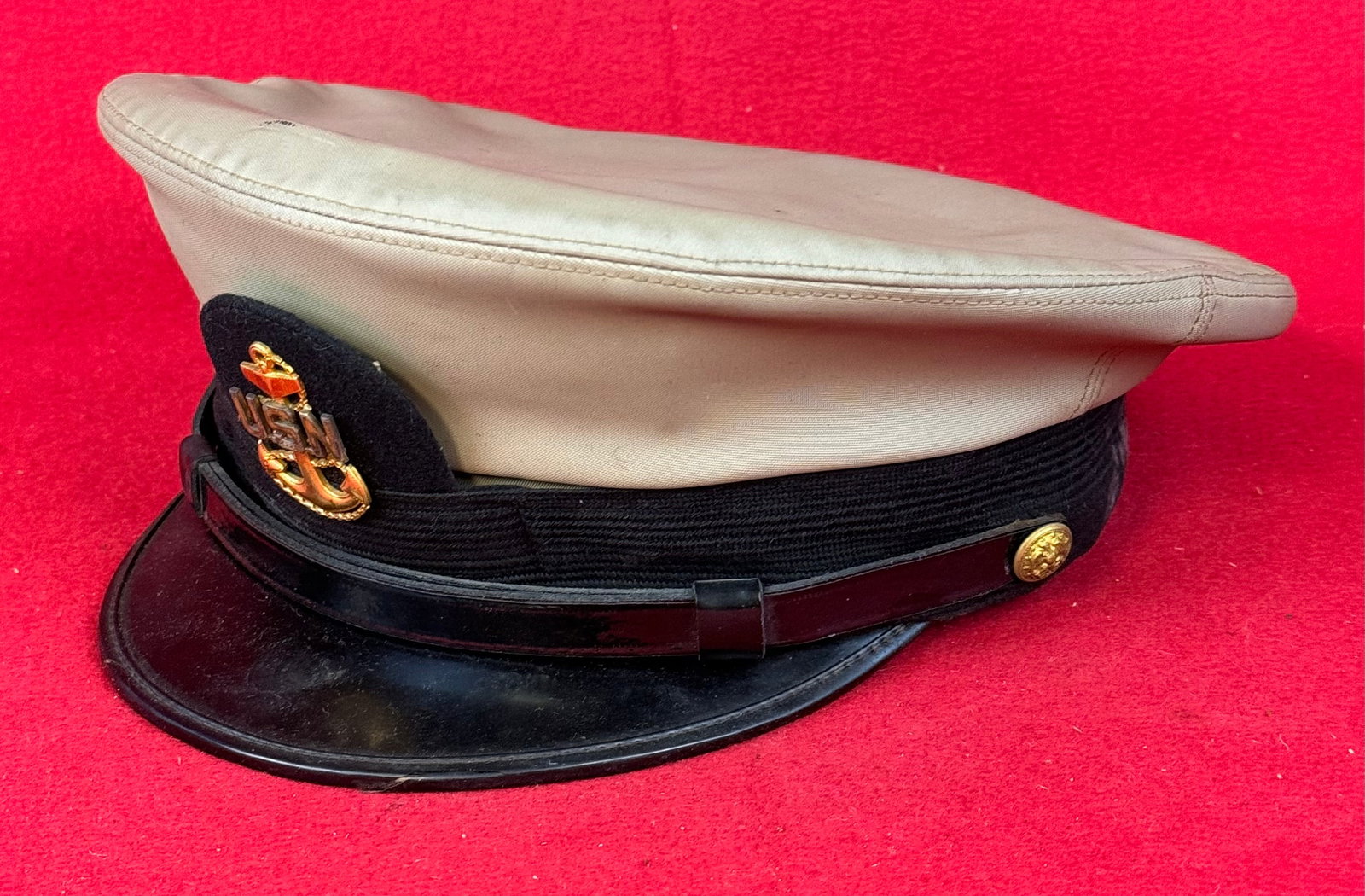 WW2 US Navy Visor Cap: World War Two United States Navy visor cap with light olive green rubberized cloth covering and a gilt metal device with anchor and U.S.N. at front. Cap was made by Bancroft Caps and is in fine condit