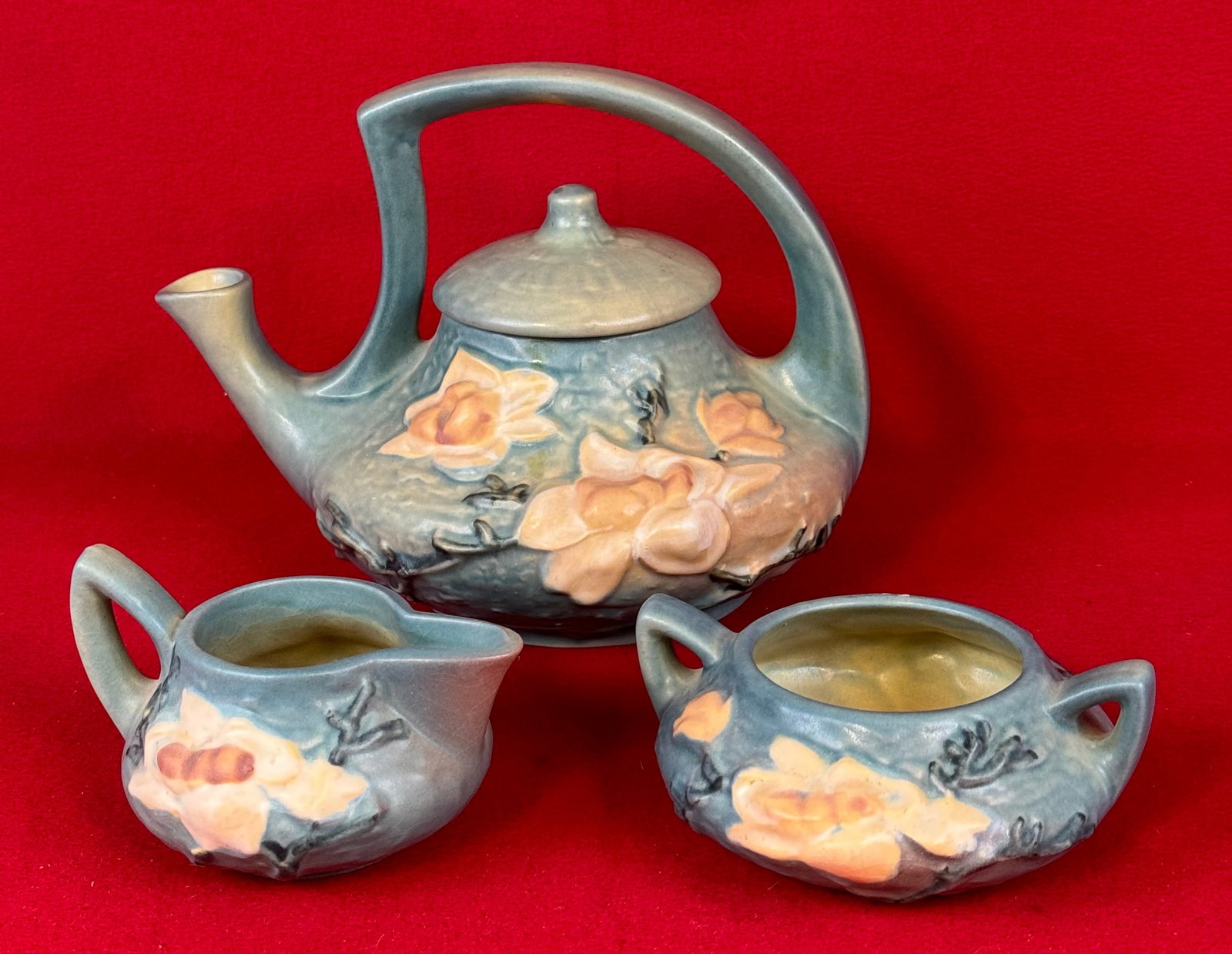 Roseville Blue Magnolia Pair Teapot, Creamer & Sugar: Original Roseville tea set to include teapot, creamer and open sugar in the Magnolia pattern which dates to 1943. Teapot is marked on underside of the base in relief Roseville / U.S.A. / 4 and the cre