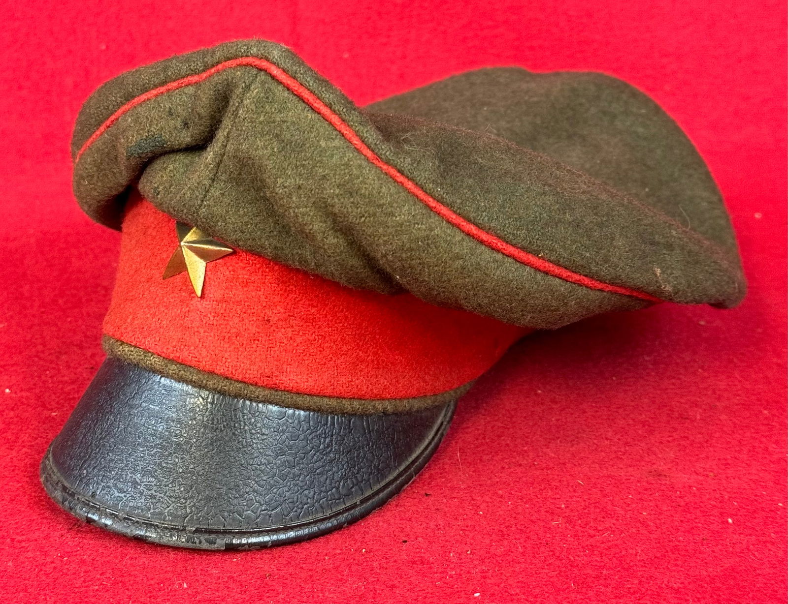 WW1 Era Imperial Japanese Olive Wool Cap: World War One era (1918) Imperial Japanese dark olive green wool cap with red felt band and red pipping at crown and having a black leather visor. Cap carries a stamped brass five pointed star insigni