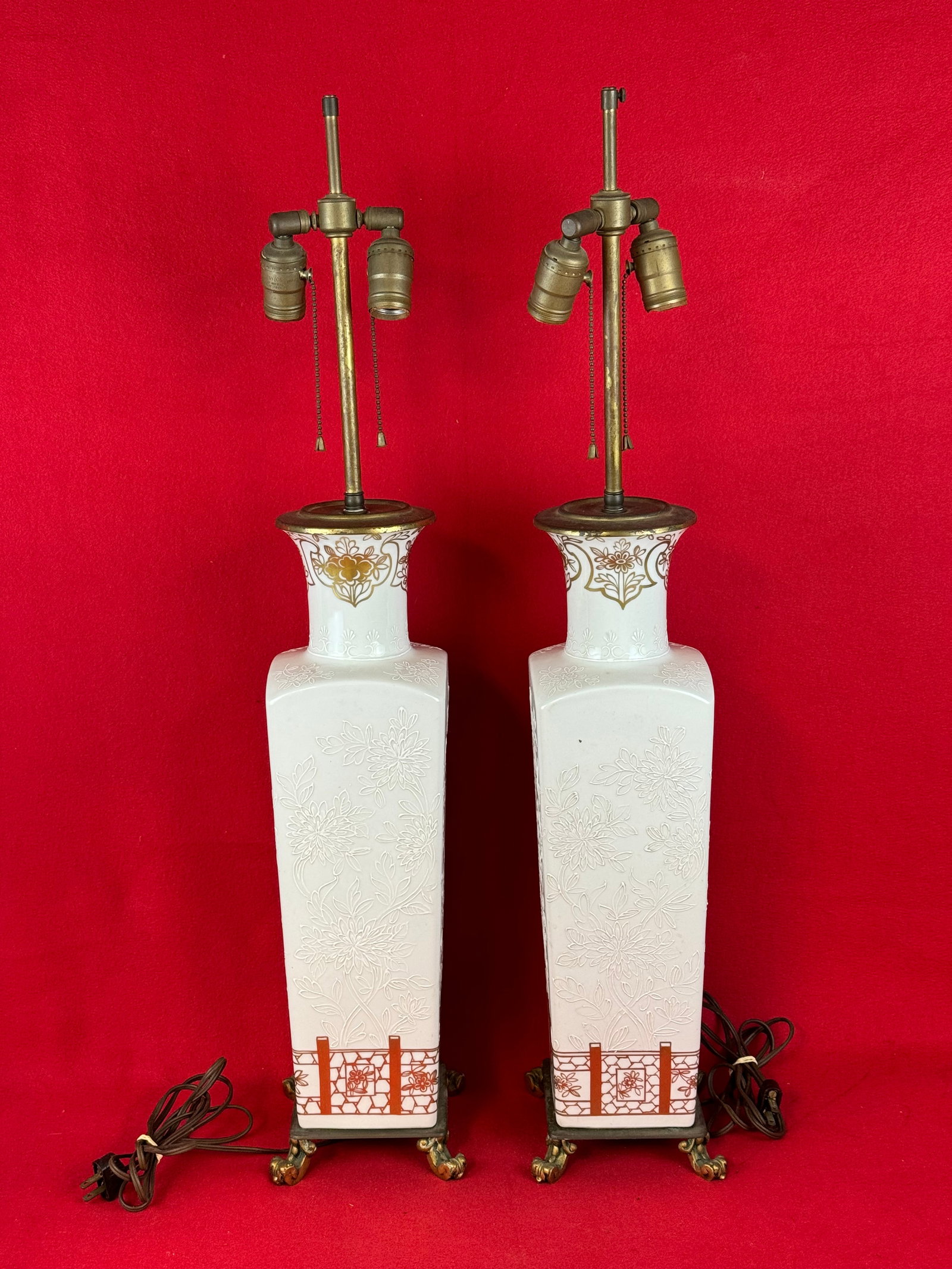 Pair Ornate French Porcelain Electric Lamps: Pair of elegant old French porcelain electric lamps with ornate bronze feet. Porcelain have delicate florals embossed on the sides and there is fire gilt decoration at the bases and near the top. Lamp