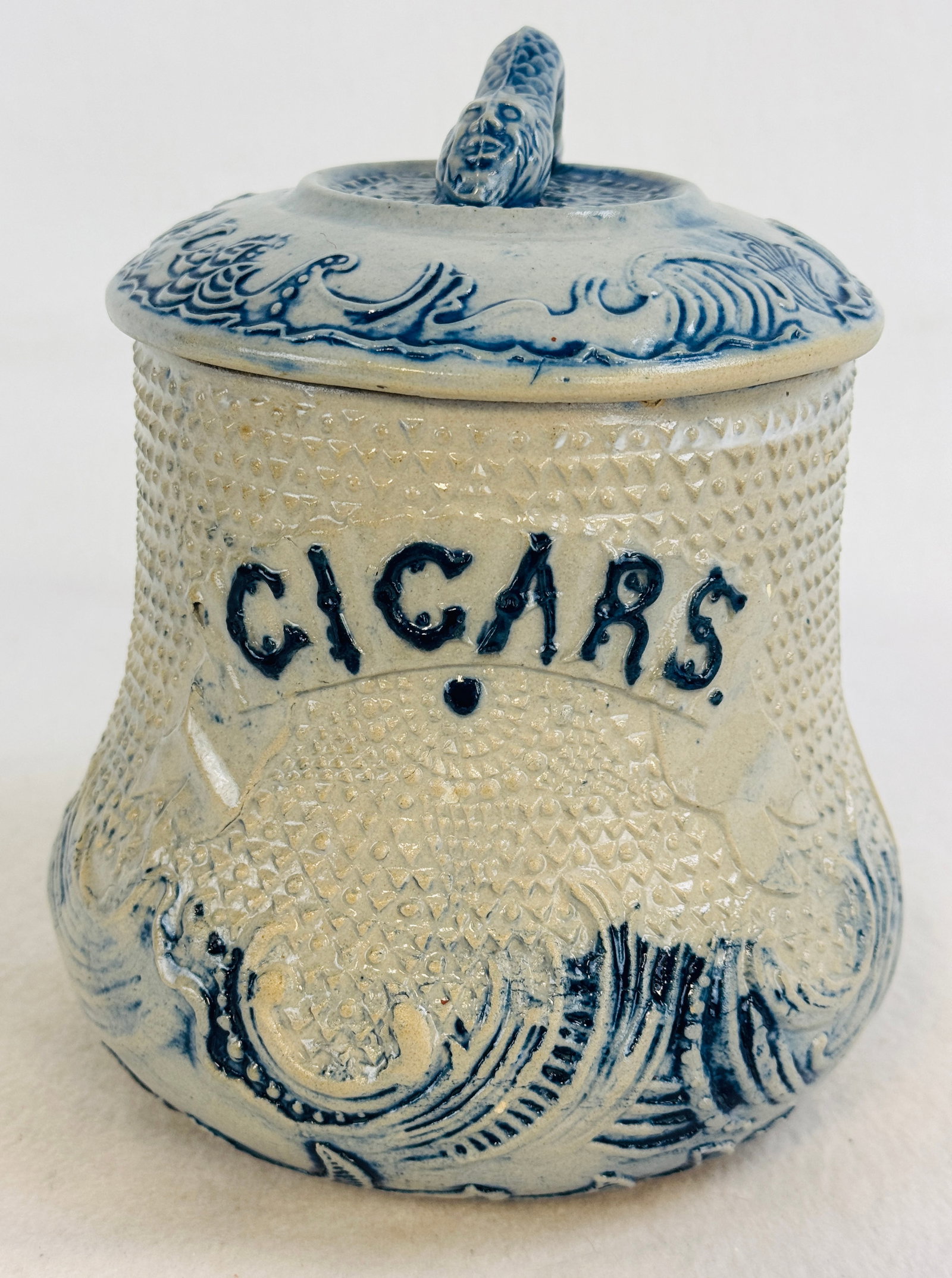 Whites Utica Bl & Wh Stoneware Cigar Humidor: 7 1/2" blue and white molded stoneware cigar humidor which was made at the Whites Pottery Utica New York. Humidor has CIGARS embossed on the front and there is a sea serpent figural finial on lid. Con