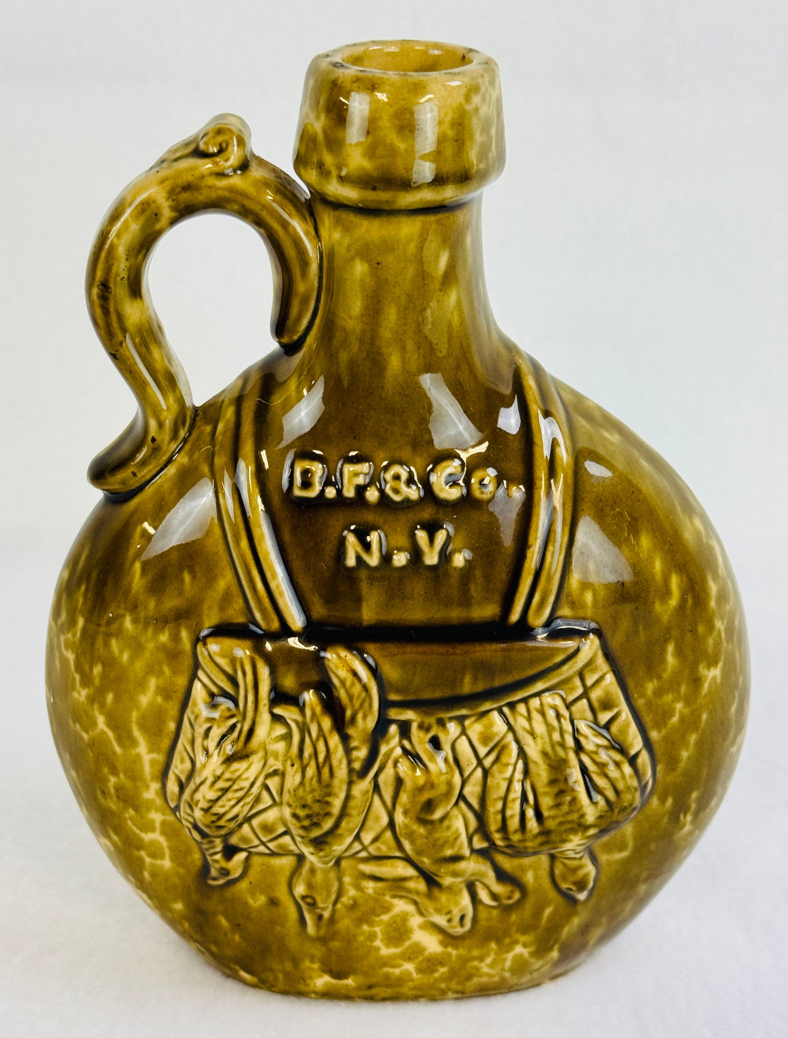 Buckley Fiske & Co N.Y. Pottery Flask: 7 1/4" pottery whiskey flask for Buckley Fiske & Co New York which has flattened sides and is embossed with a game bag on one side and having hunting dogs with rifle depicted on the other. Flask is em