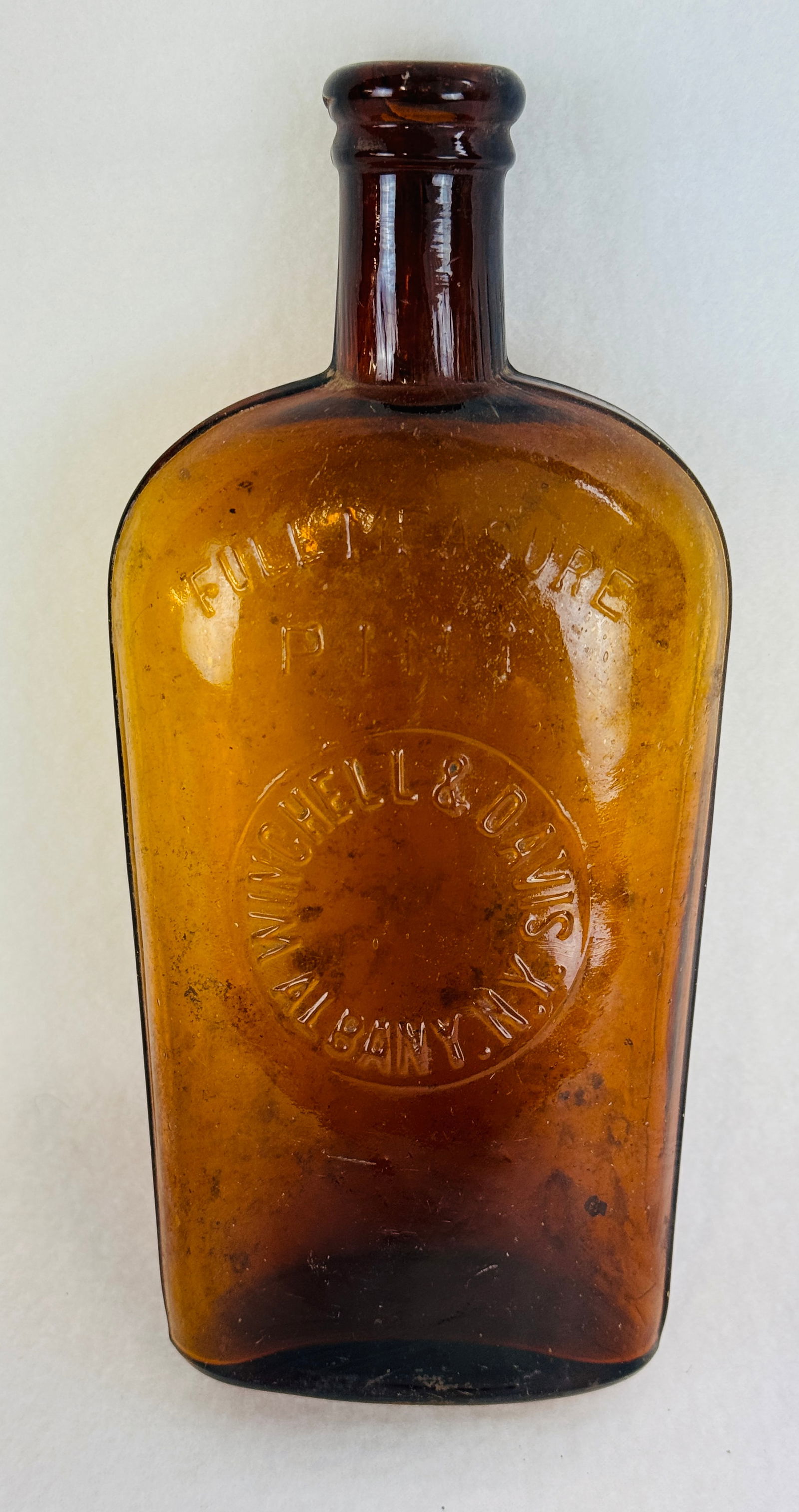 Winchell & Davis Albany Amber Strap Sided Flask: 8 1/2" blown in mold with tooled lip amber strap sided flask which is embossed at the front in a round slug plate Winchell & Davis Albany N.Y.. Condition - dug bottle with surface wear and both intern