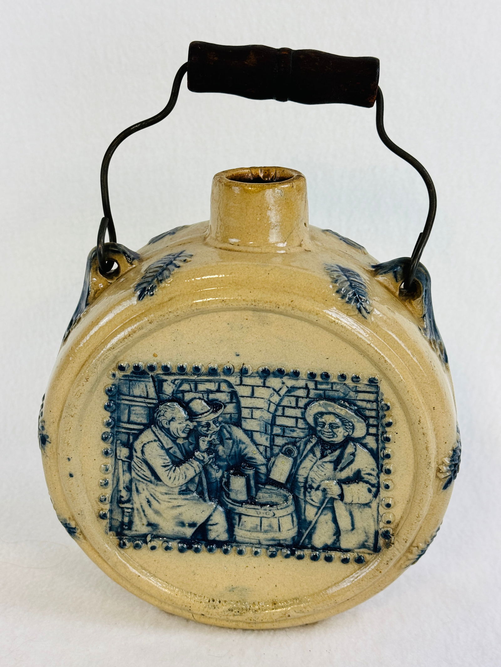 Blue & White Molded Stoneware Canteen: 7 3/4" tall 6 1/2" diameter blue and white molded stoneware canteen with its original black painted wood and wire bail handle. The canteen has a scene of men drinking around a barrel while the other s