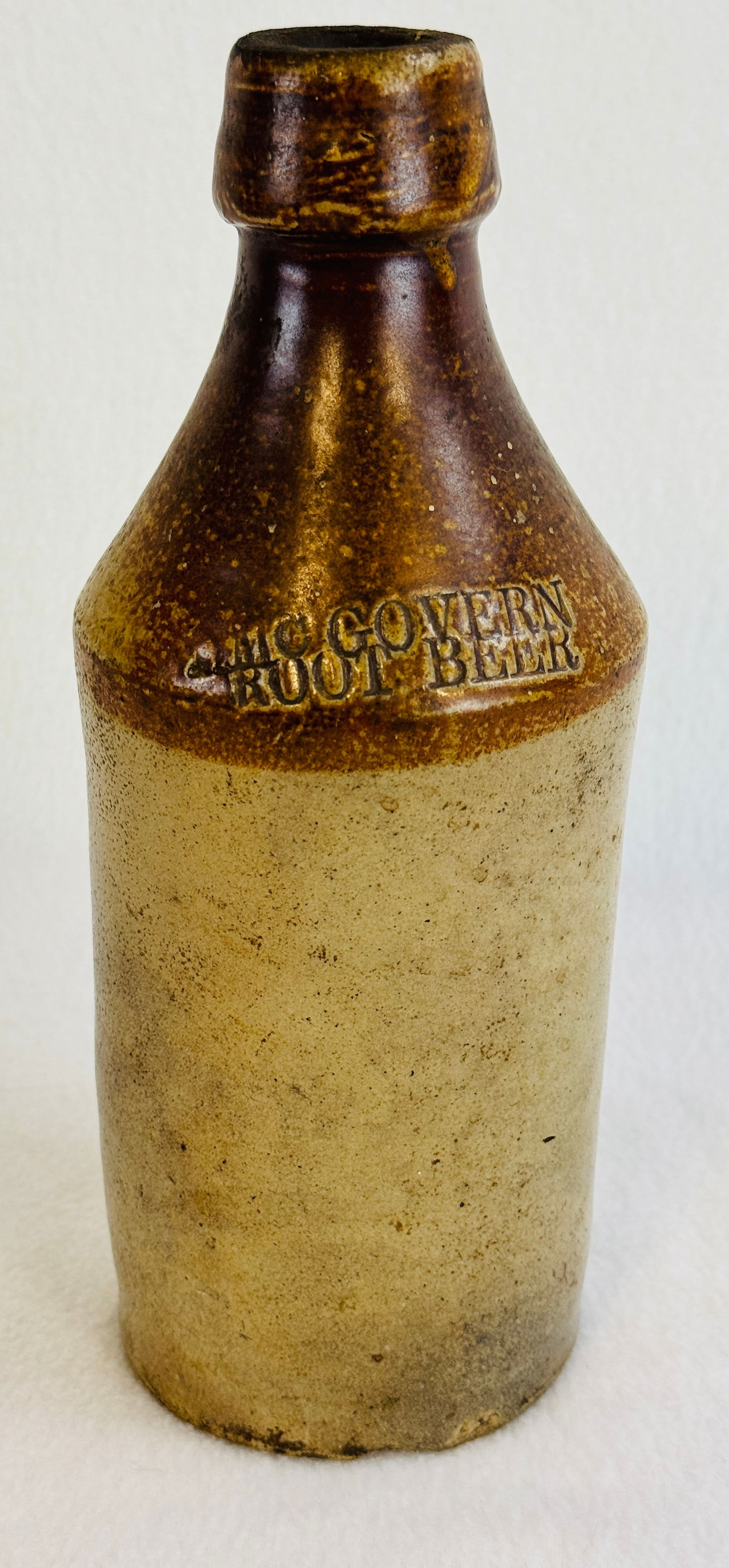 T. McGovern Root Beer Stoneware Bottle: 9 3/4" stoneware bottle which is impressed at the shoulder T McGovern / Root Beer and has a ochre decorated top and shoulder. Condition - large chip to underside of base and a chip at shoulder on reve