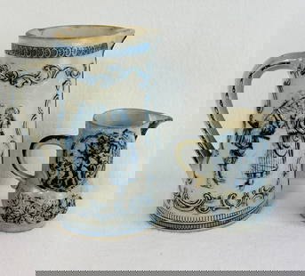 Lot 2 Blue & White Molded Stoneware Pitchers: Lot of two blue and white molded stoneware pitchers both most likely produced by the Whites Pottery Utica New York. The taller pitcher measures approximately 9" and depicts one older and one younger c